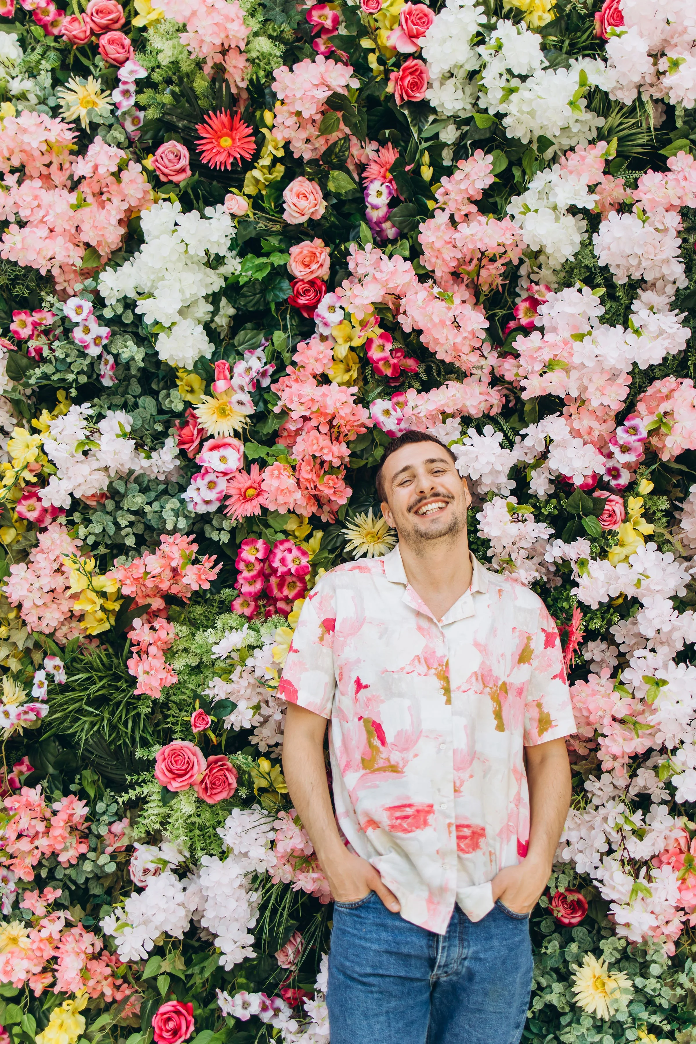 Pesojoonas hymyilee ja seisoo kukkivien värikkäiden kukkien edessä, jotka muodostavat taustan.