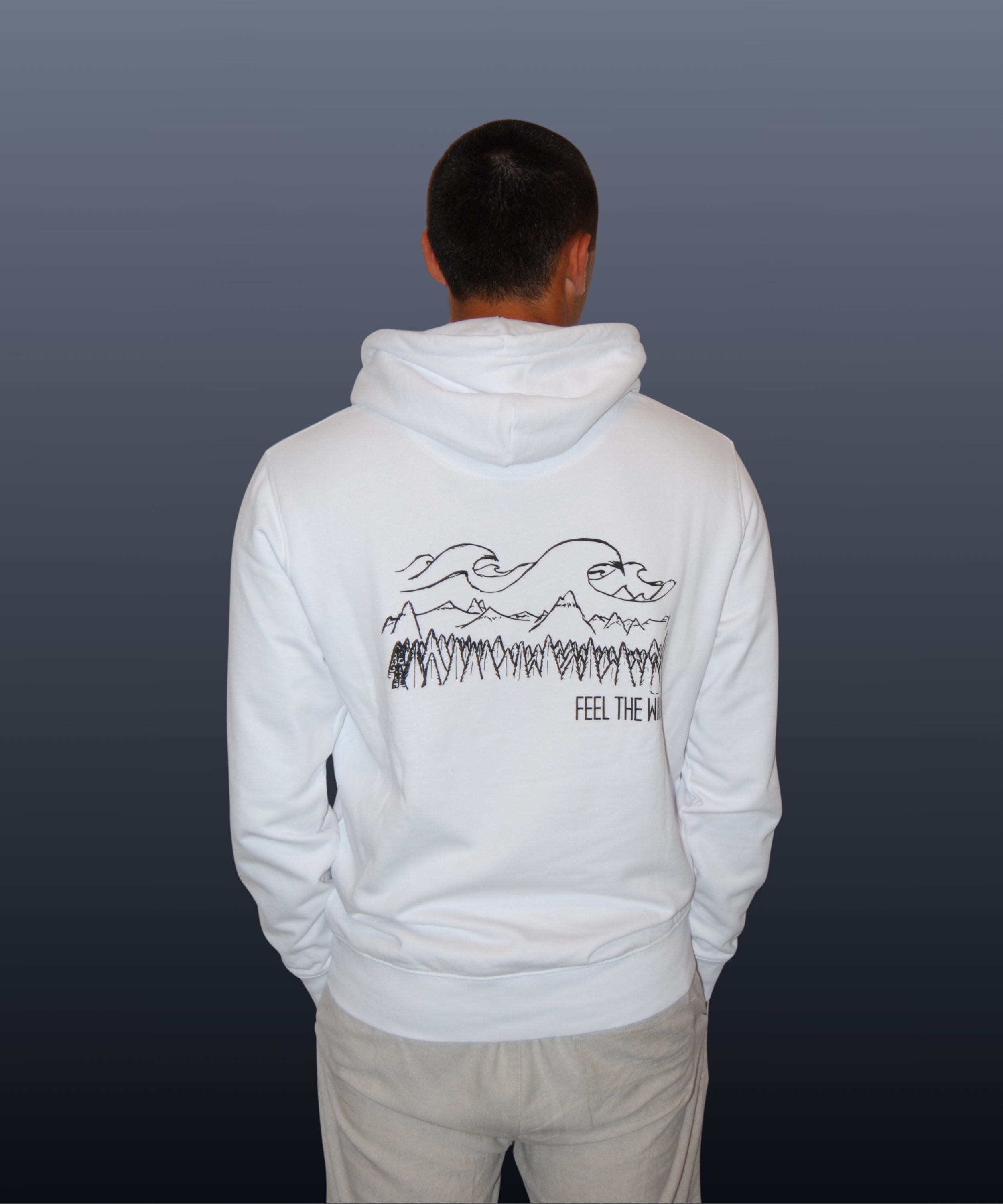 Una persona vista di schiena, indossa una felpa bianca con una grafica di montagne, nuvole e alberi, con la scritta 'FEEL THE WILD'.