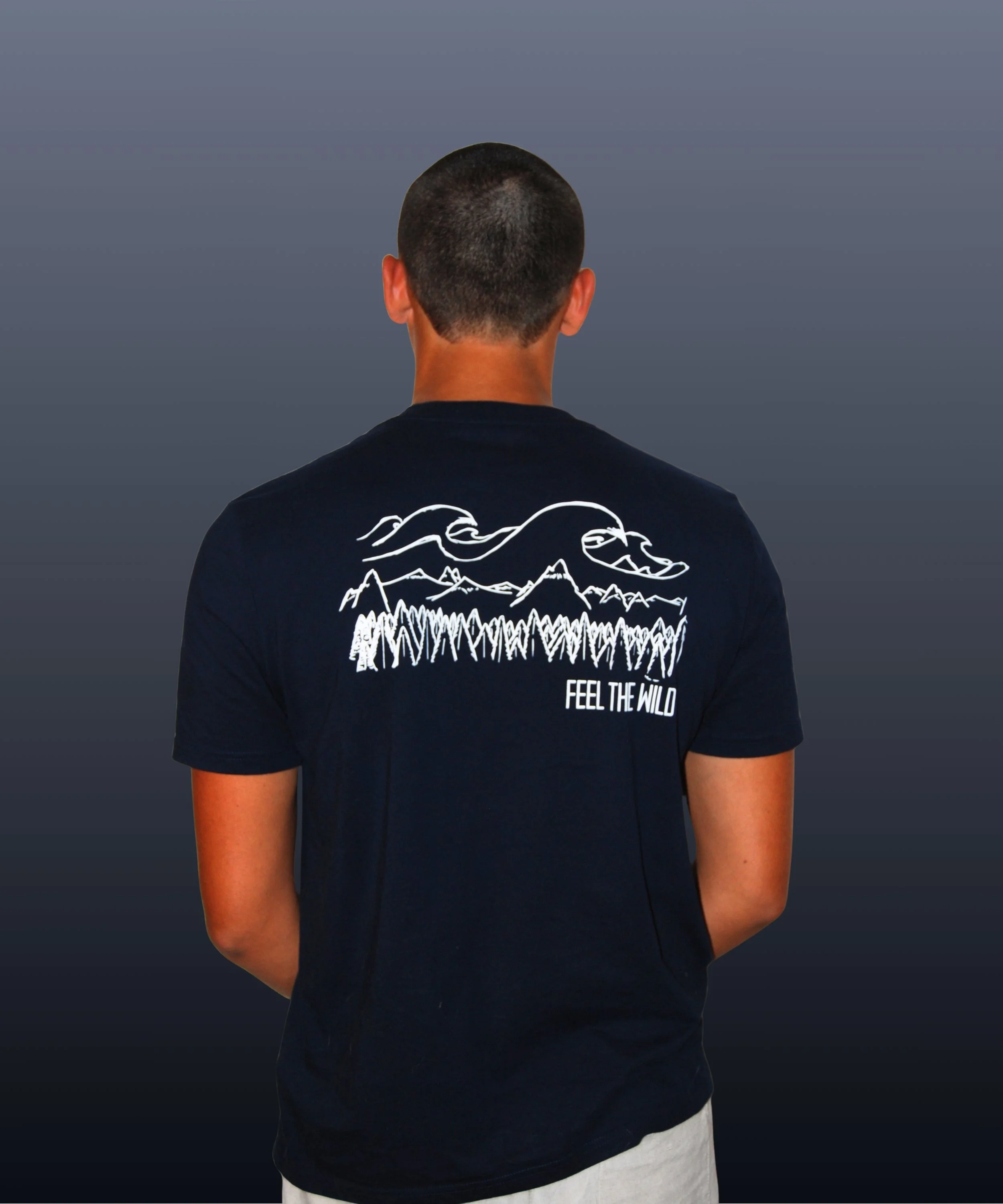 Persona vista di schiena che indossa una maglietta nera con disegno di montagne, alberi e nuvole stilizzati, con la scritta 'FEEL THE WILD'.
