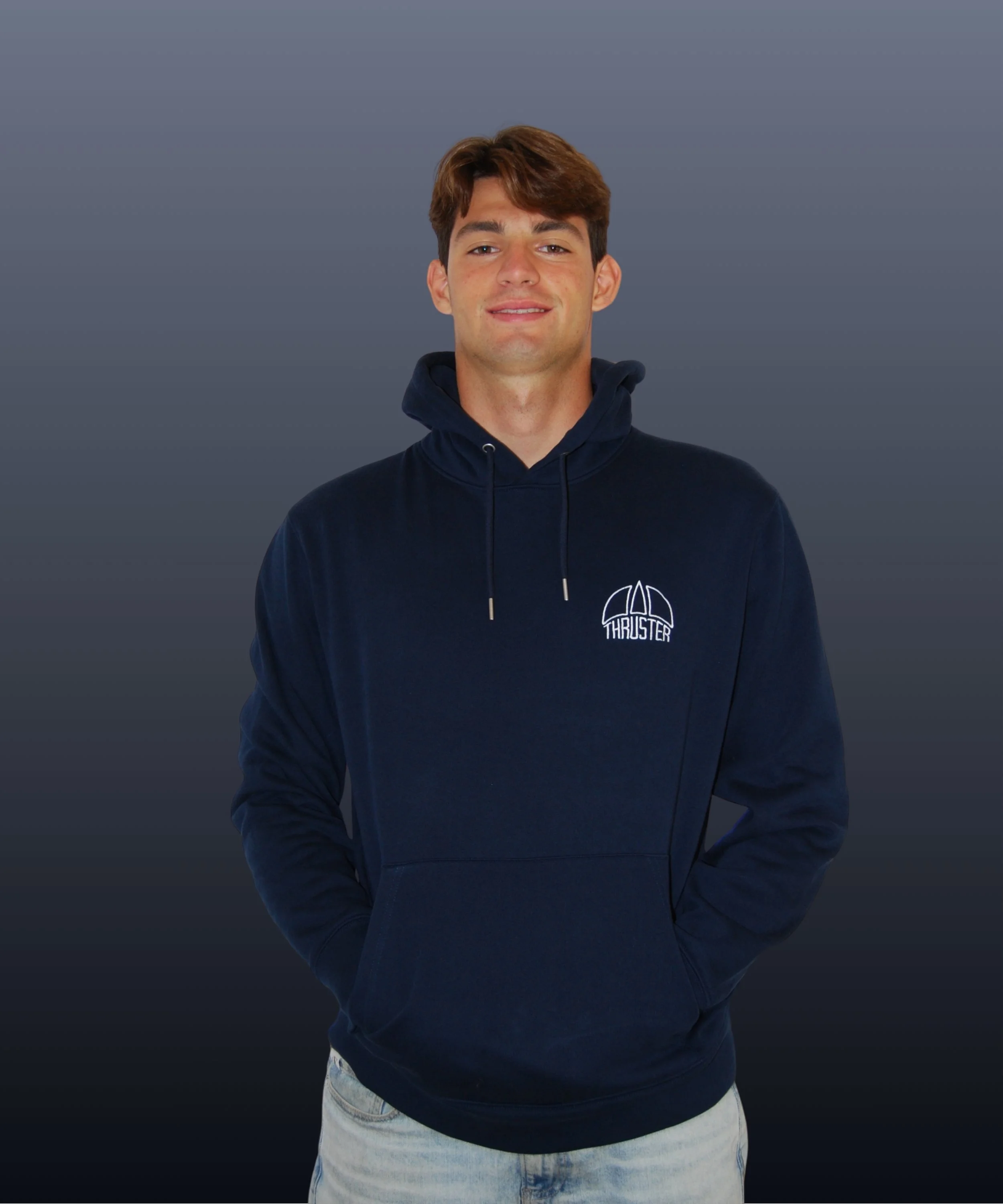 Giovane uomo con capelli castani, sorriso, indossa felpa blu con cappuccio e logo "Thruster", sfondo grigio.