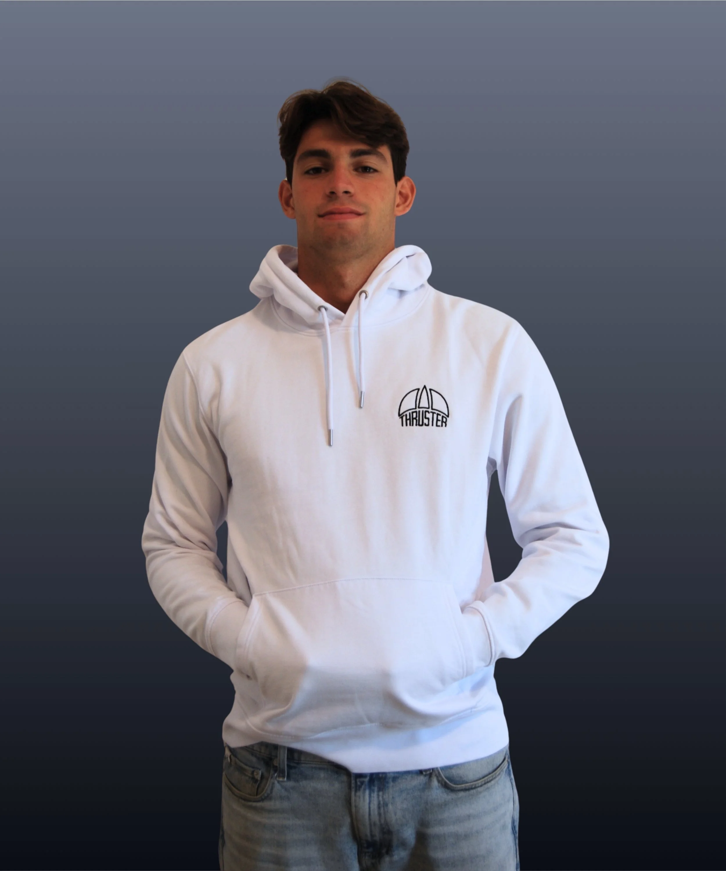 Giovane uomo con capelli castani, indossa felpa bianca con logo 'Thruster' e jeans, sfondo grigio scuro.