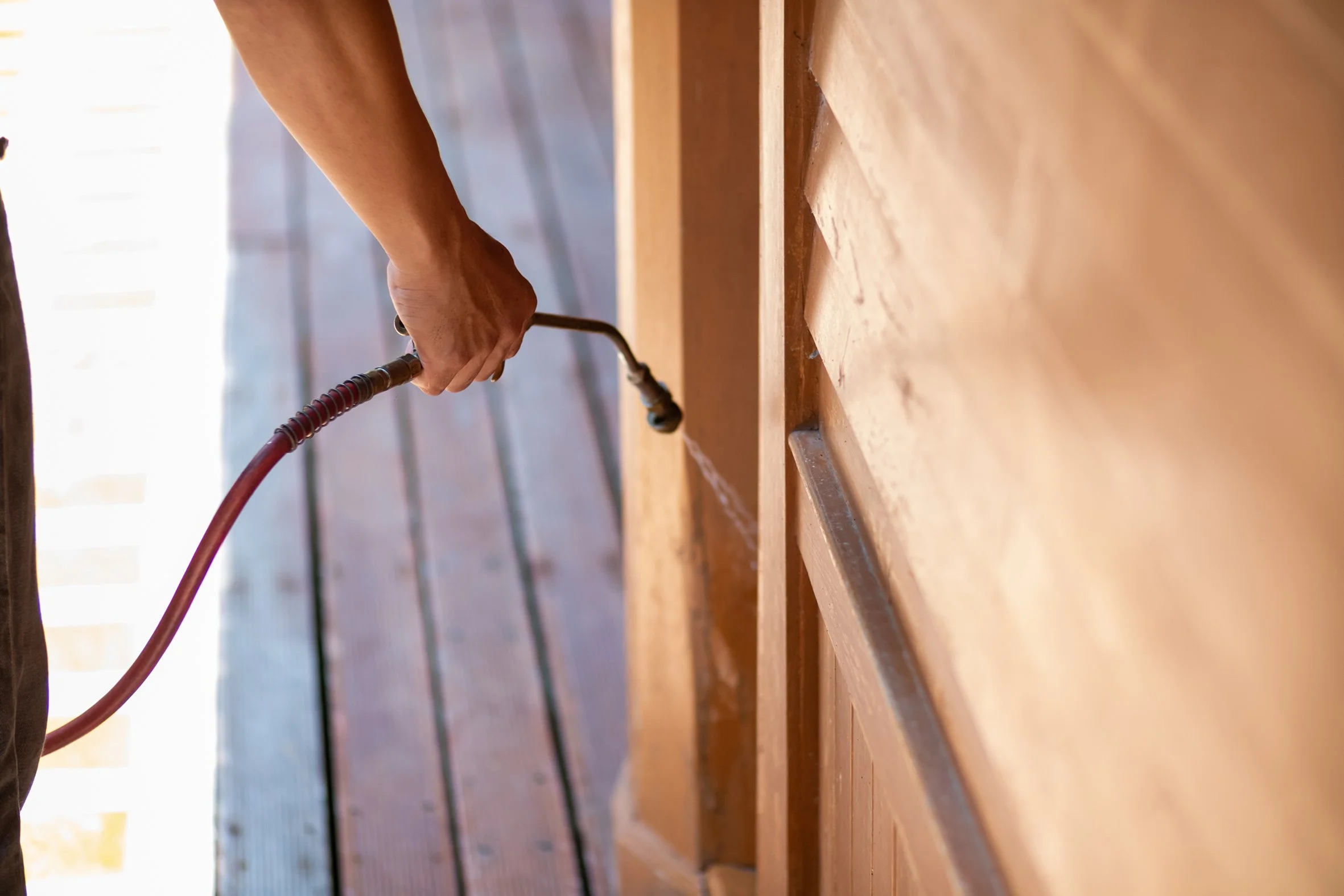 A person using a spray gun to apply finish to wooden furniture or cabinetry in a woodworking shop.