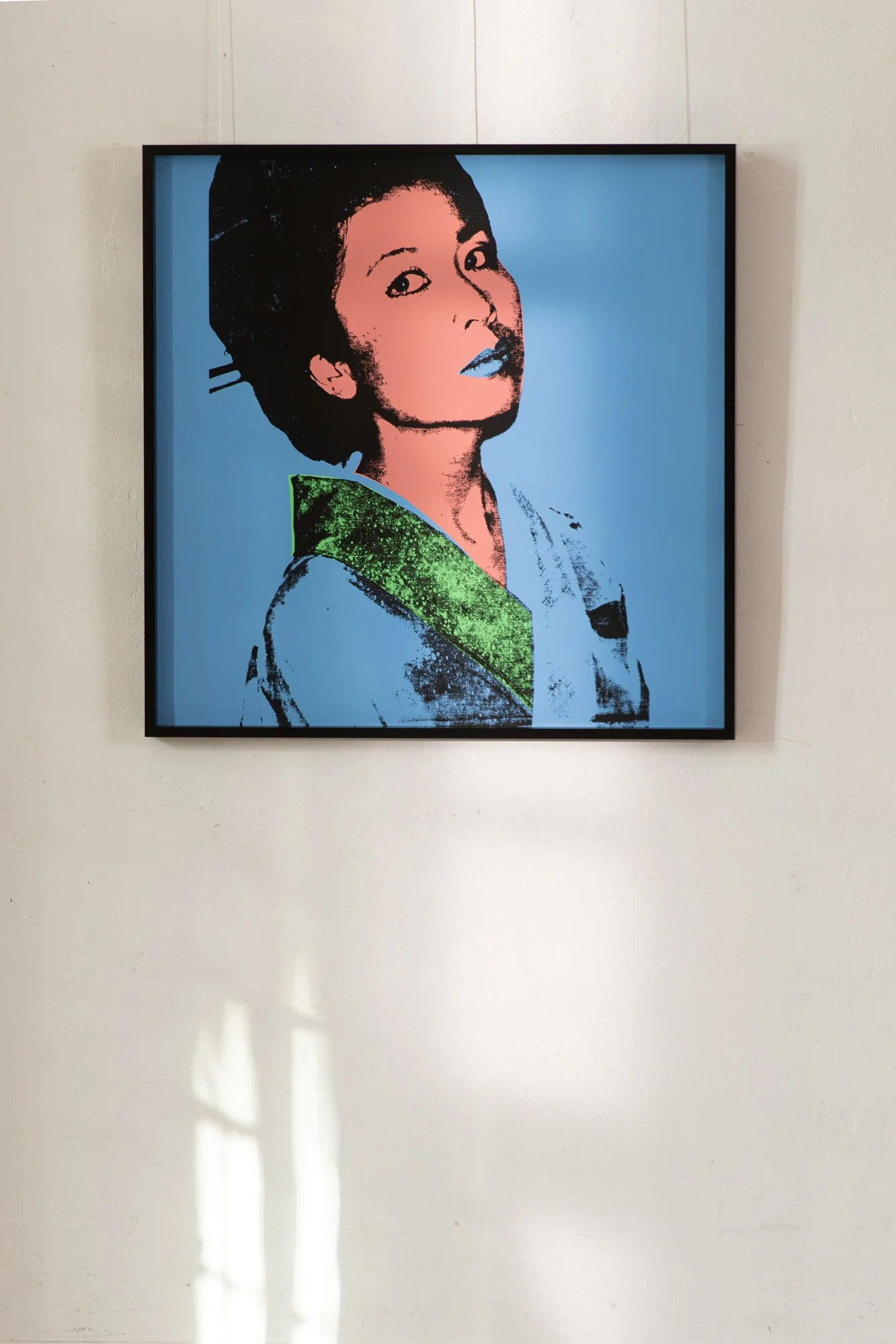 Grafika „Kimiko” Andy'ego Warhola eksponowana w ręcznie wykonanej ramie z hebanu gabońskiego, na tle jasnej ściany.