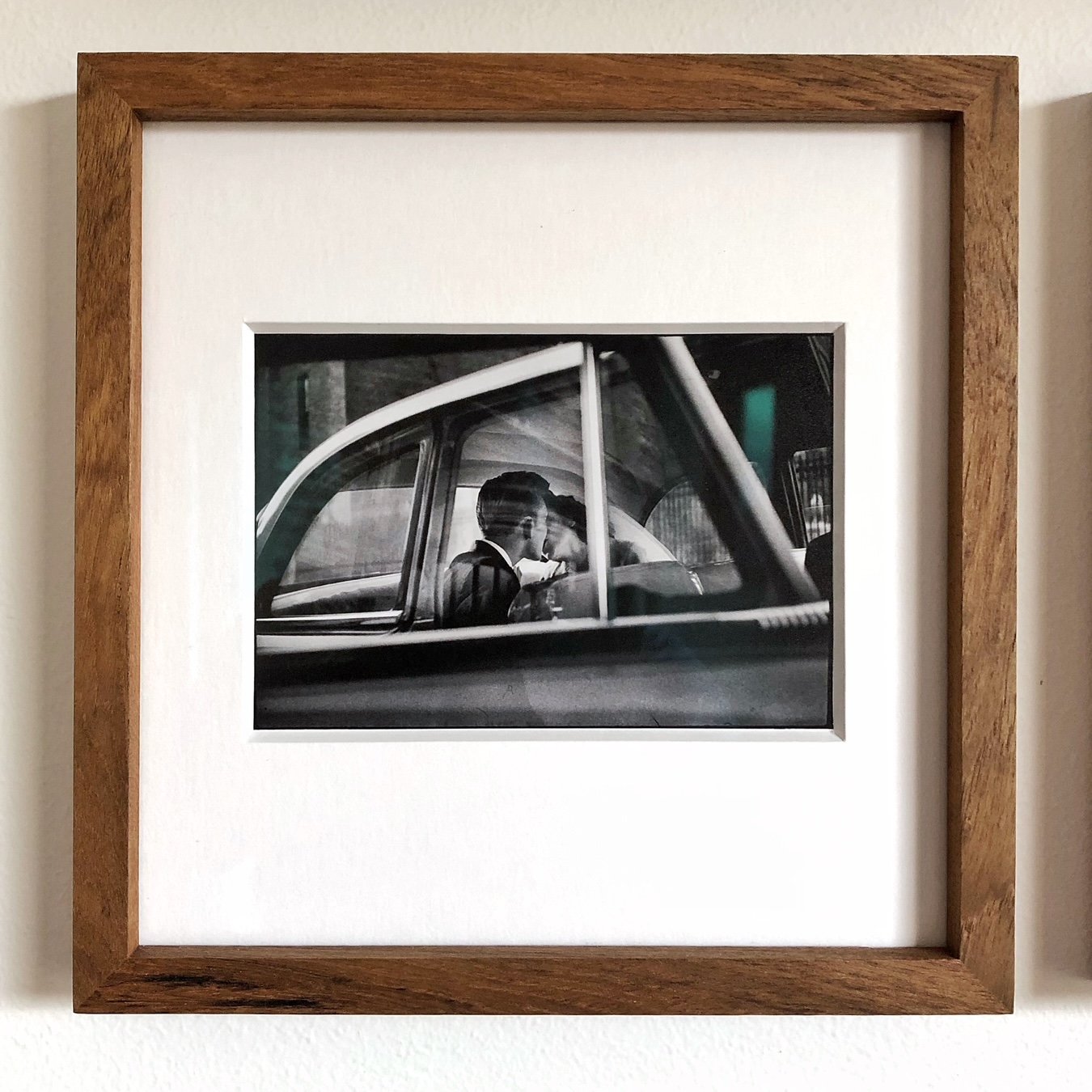Black and white photograph of a couple sitting closely in the backseat of a vintage car, sharing an intimate moment.