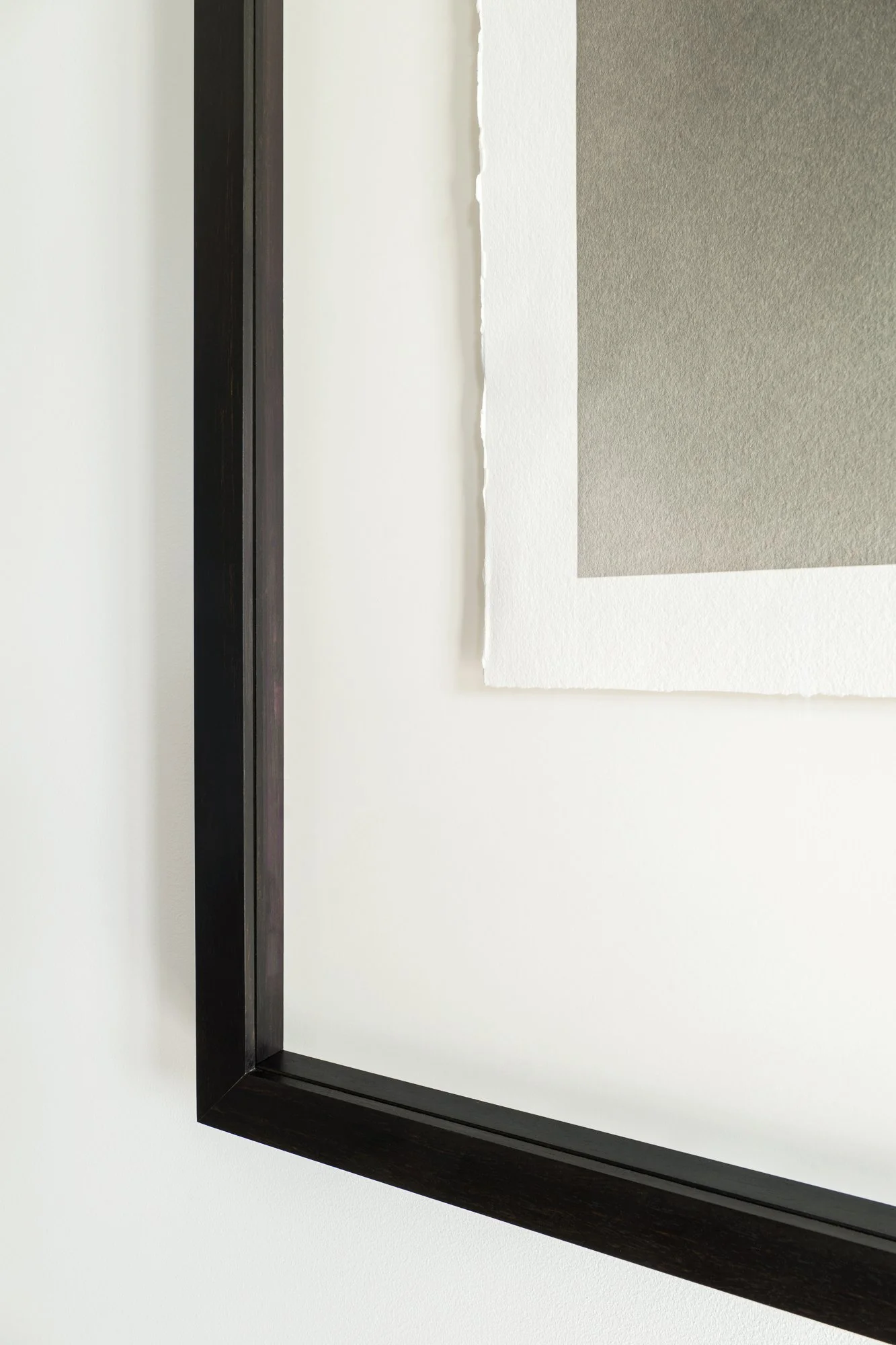 Close-up of a black photo frame hanging on a white wall, with a white matte and gray background inside the frame.
