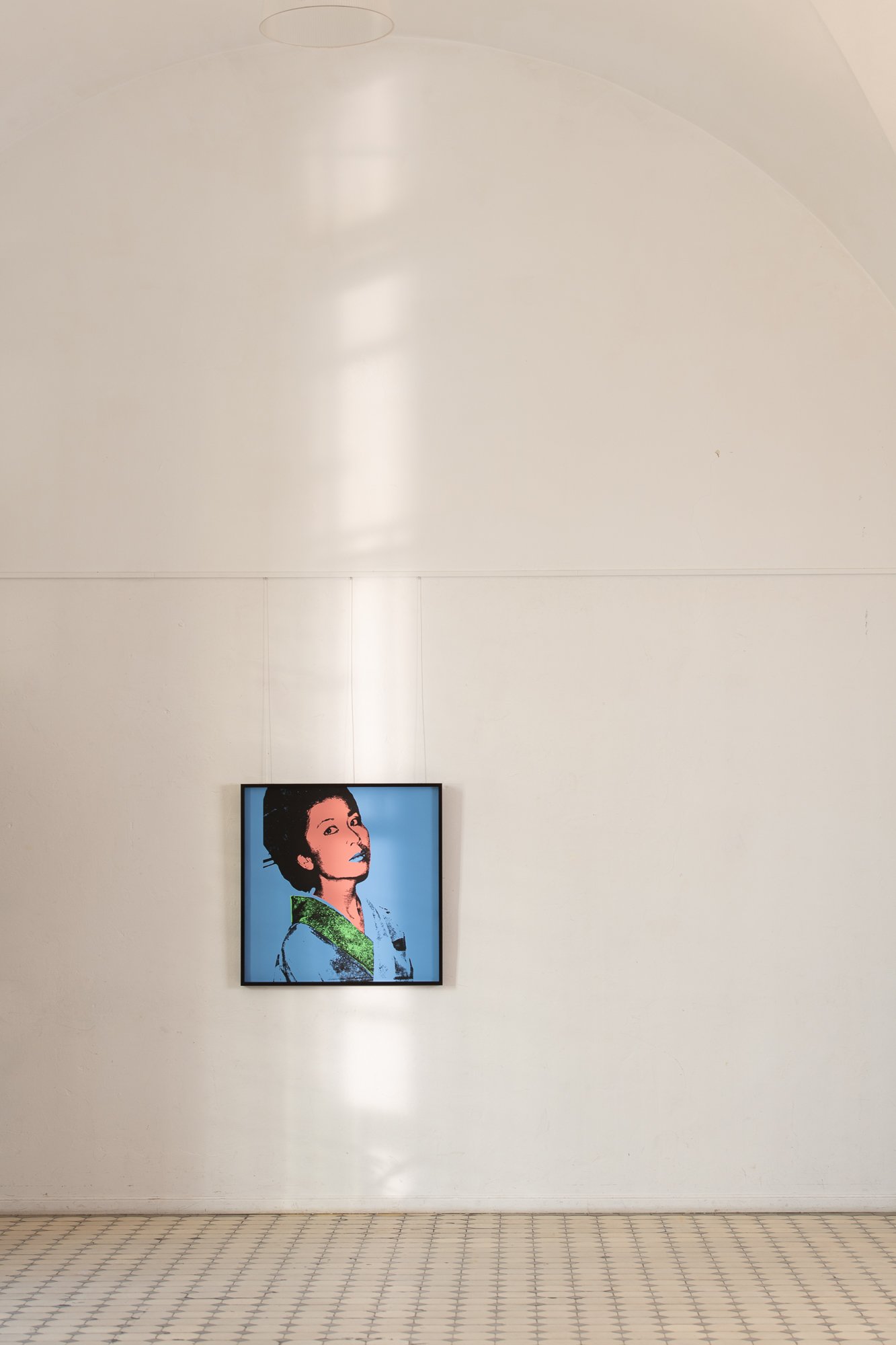 Grafika „Kimiko” Andy'ego Warhola w ręcznie wykonanej ramie z hebanu gabońskiego podczas ekspozycji na jasnej ścianie, w pomieszczeniu wyłożonym dekoracyjnymi płytkami podłogowymi.