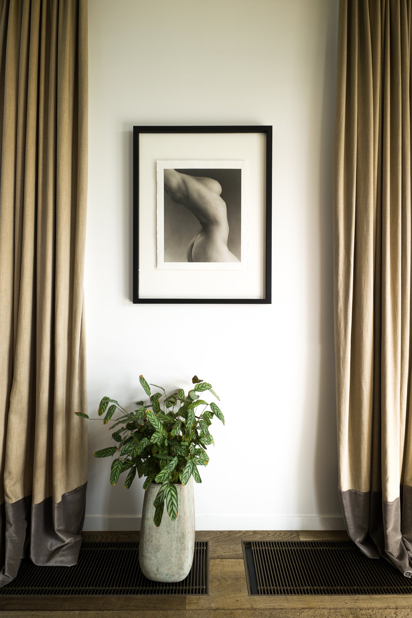 Zdjęcie Roberta Mapplethorpe'a Lisa Marie, oprawione w czarną, hebanową ramę, zawieszone na białej ścianie, pomiędzy zasłonami z beżowej tkaniny, na podłodze roślina w szarej donicy.