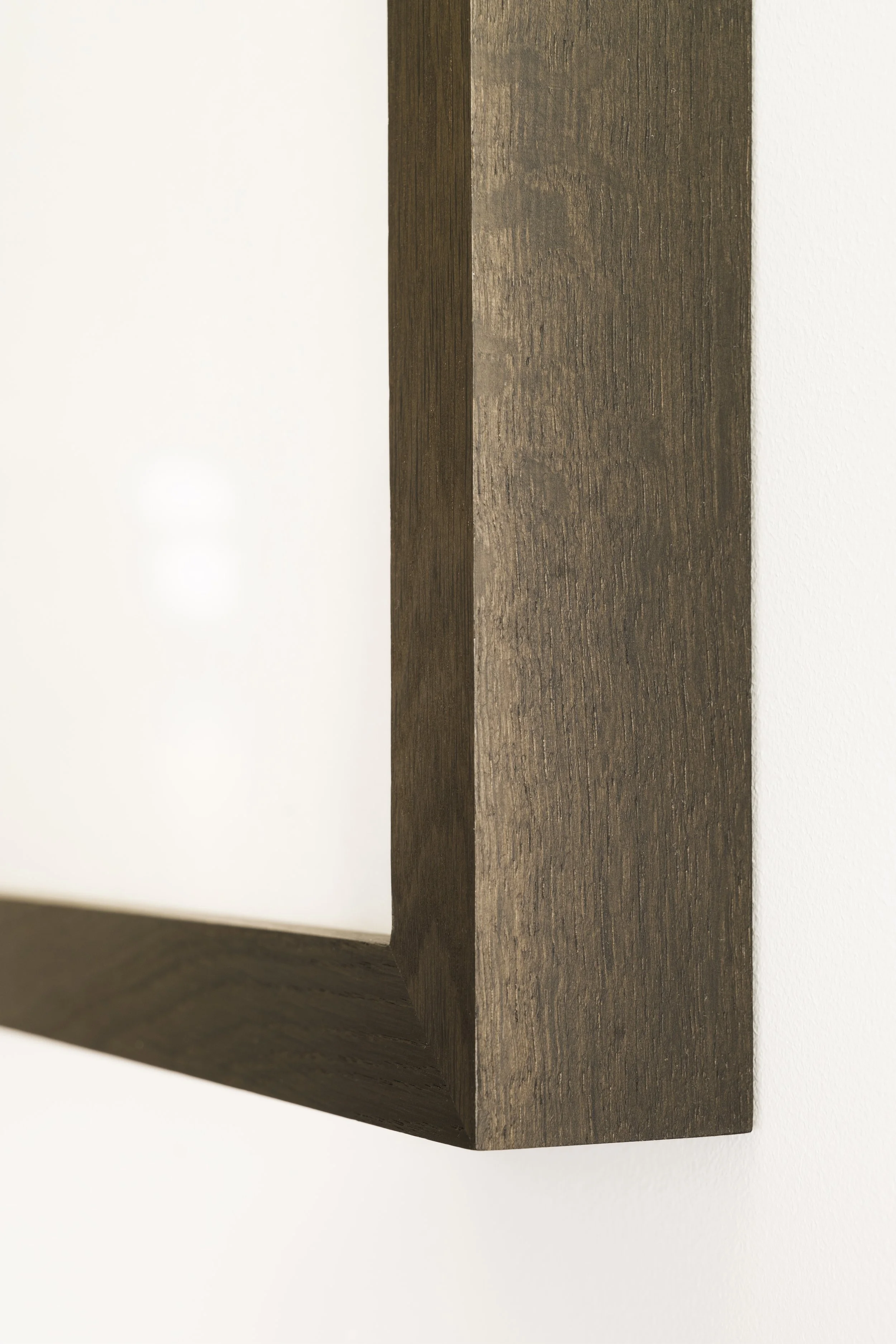 Close-up of a dark wooden corner shelf or frame against a white wall, showing texture and grain of the wood.