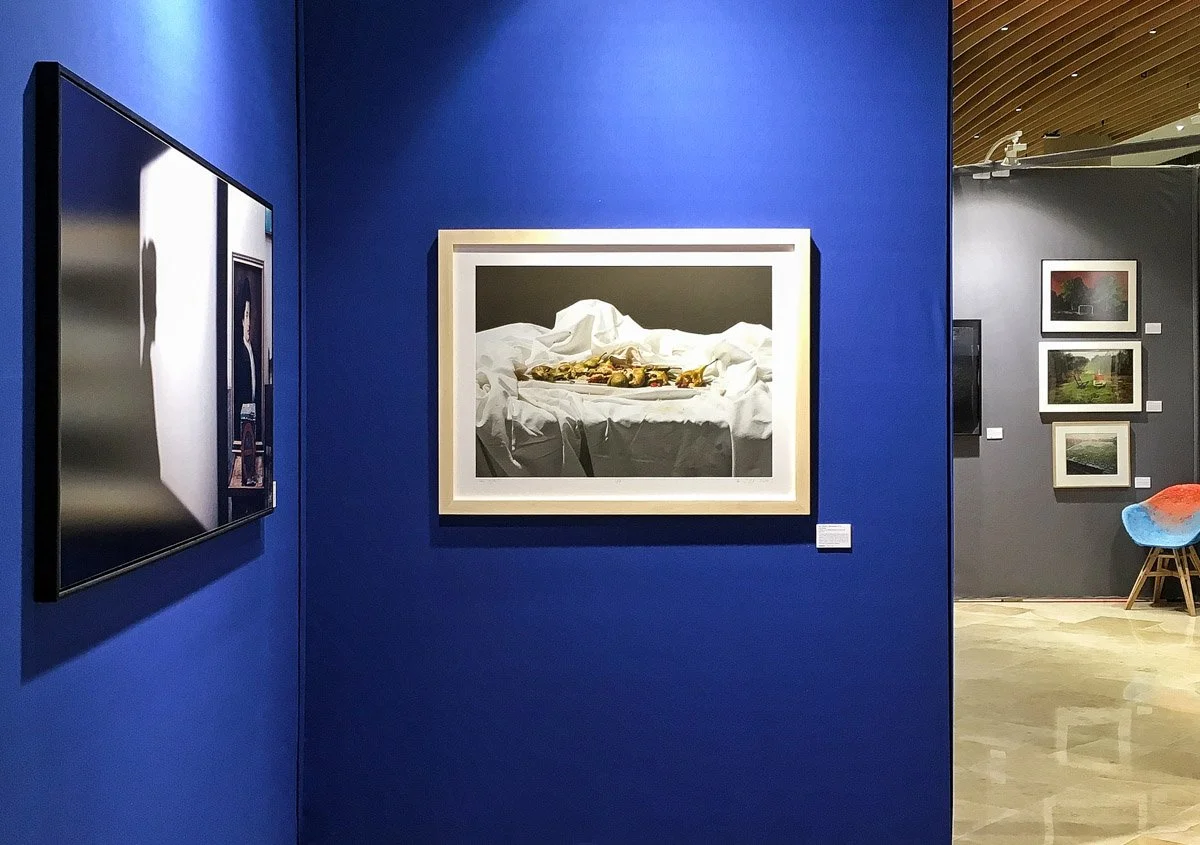 Fotografia Pawła Żaka oprawiona ramę drewnianą jasnego koloru zawieszona na jaskrawo niebieskiej ścianie galerii.