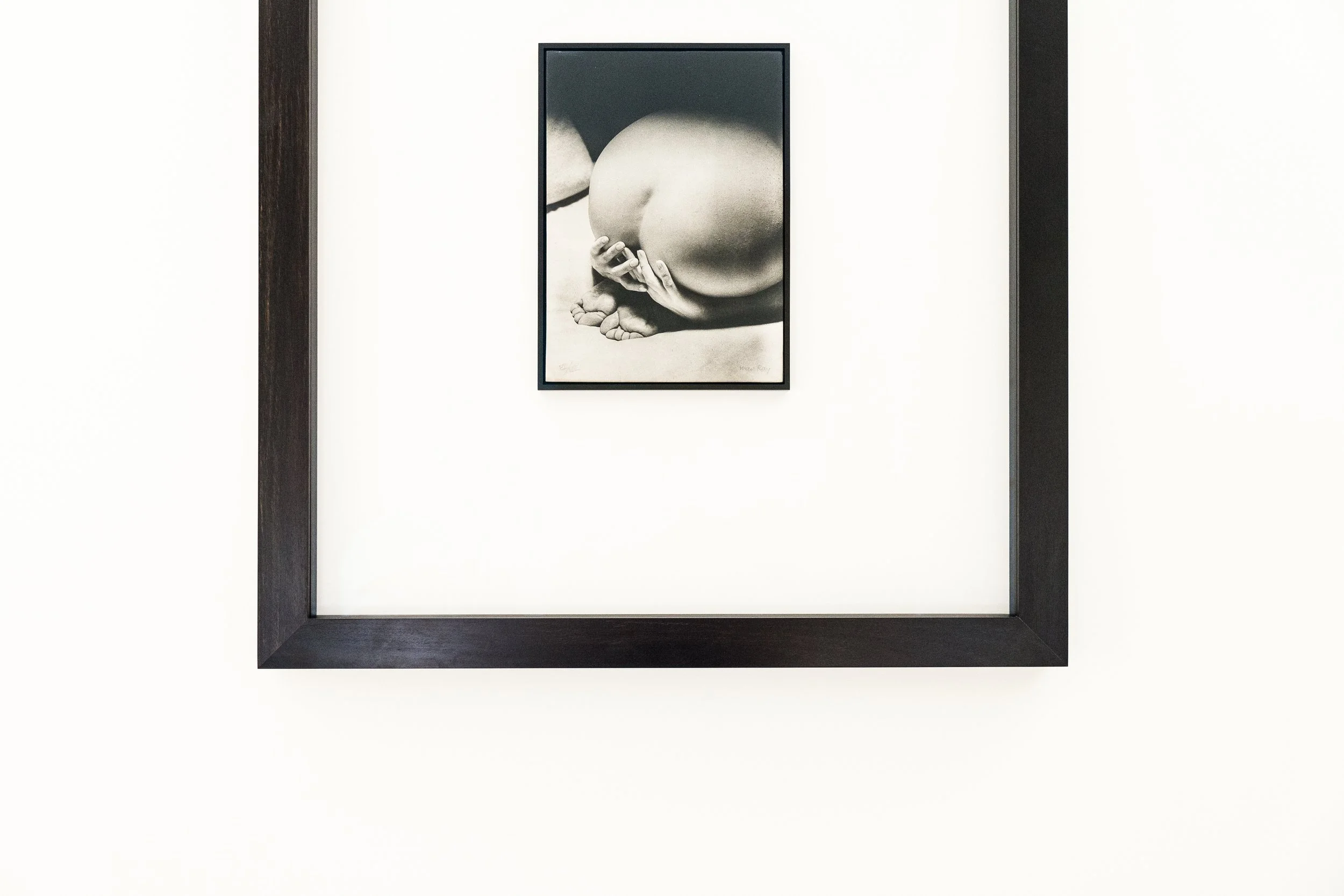 Fotografia Man Ray'a Prayer oprawiona w dwie hebanowe, czarne ramy, zawieszona na jasnej ścianie, ukazana w zbliżeniu.