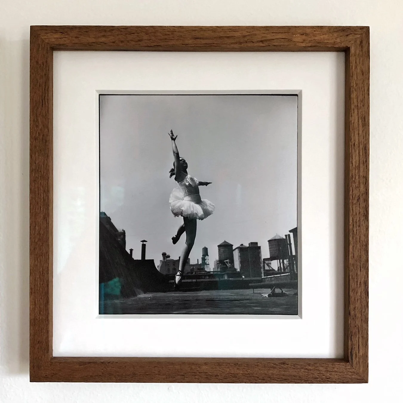 Black and white photograph of a ballet dancer jumping on a rooftop with city buildings in the background.