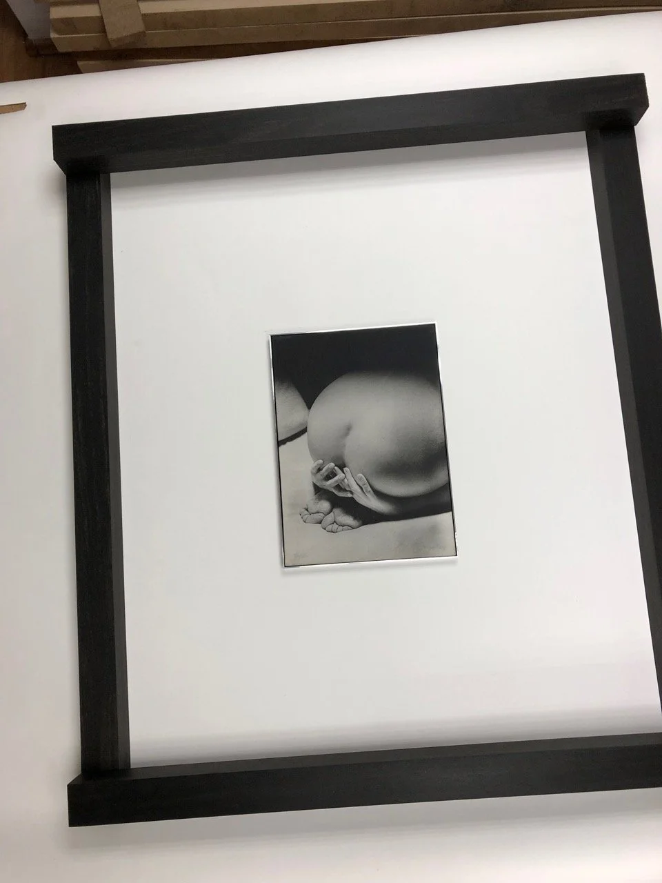 Black and white photo of a close-up of a pregnant belly with a hand resting on it, framed with a black border