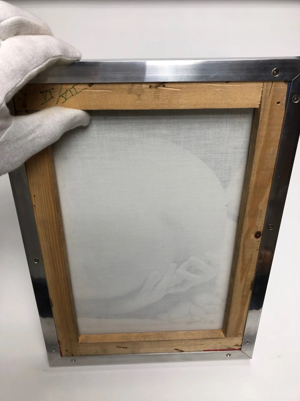 Backside of a framed canvas art, held by a person wearing a glove, showing the wooden frame and mesh canvas surface.