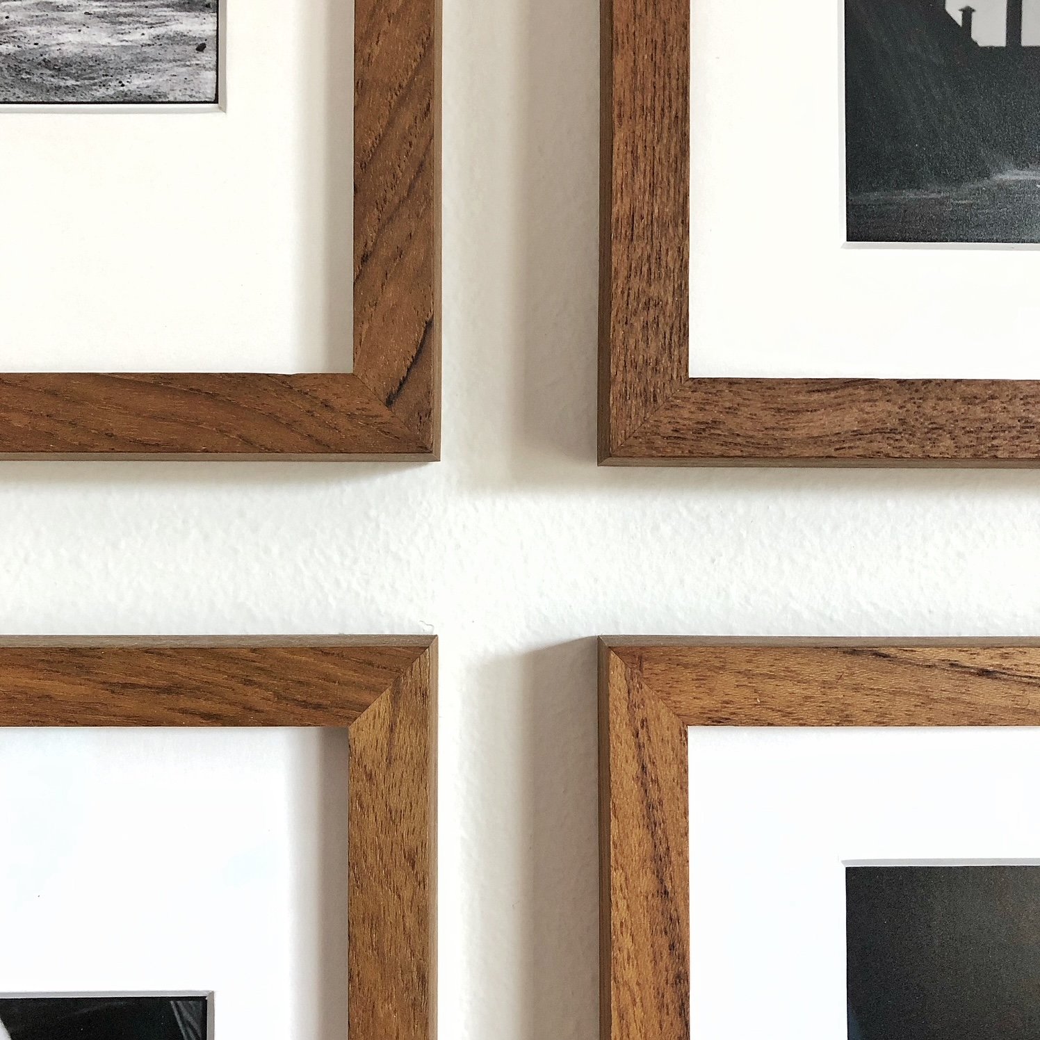 Close-up of four wooden photo frames arranged in a grid pattern on a white wall.