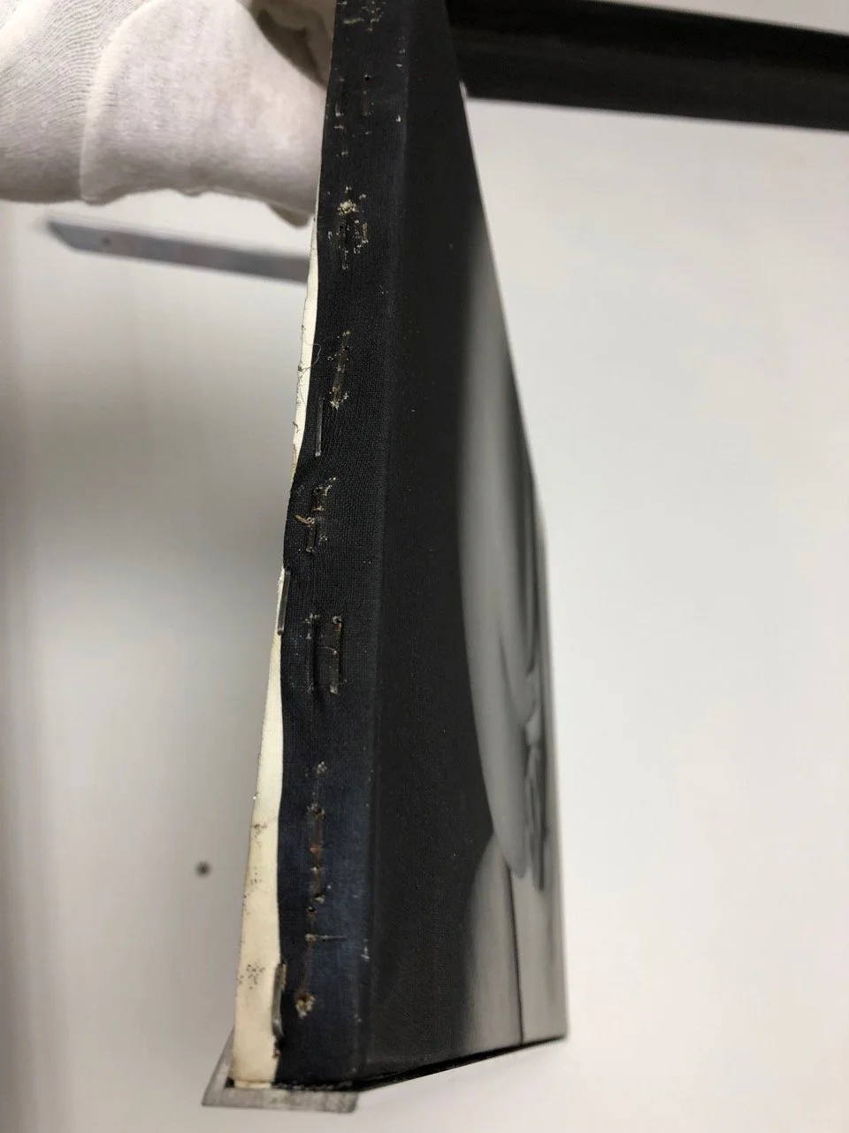 Close-up of a damaged, worn corner of a black picture frame with visible staples and chipping paint.