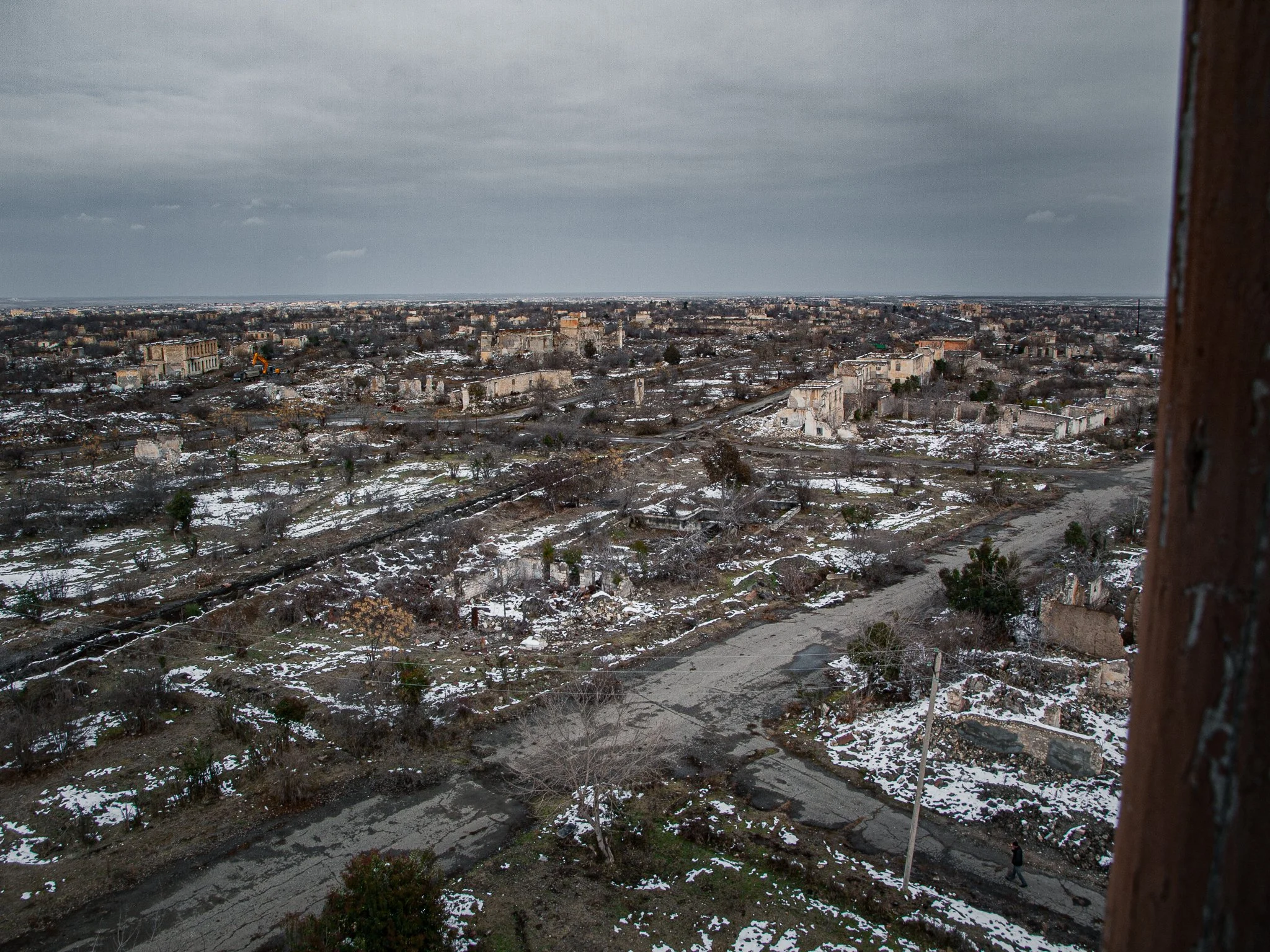 A cityscape with abandoned and destroyed buildings, snow on the ground, and a cloudy sky.