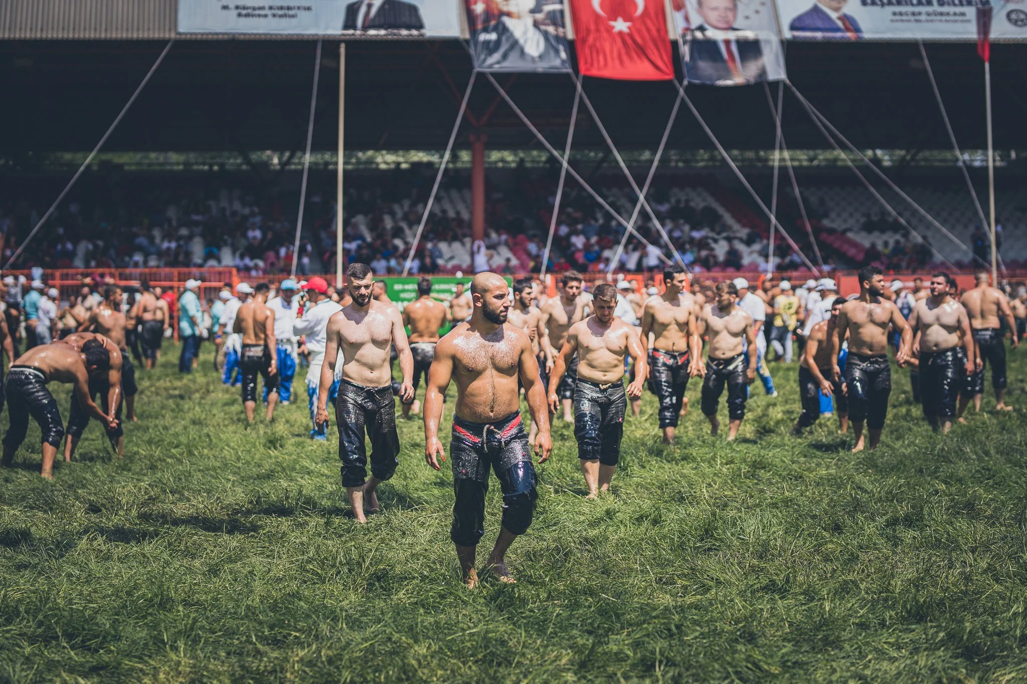 Men participating in a traditional water-splashing event on a grass field, with a crowd and banners in the background.