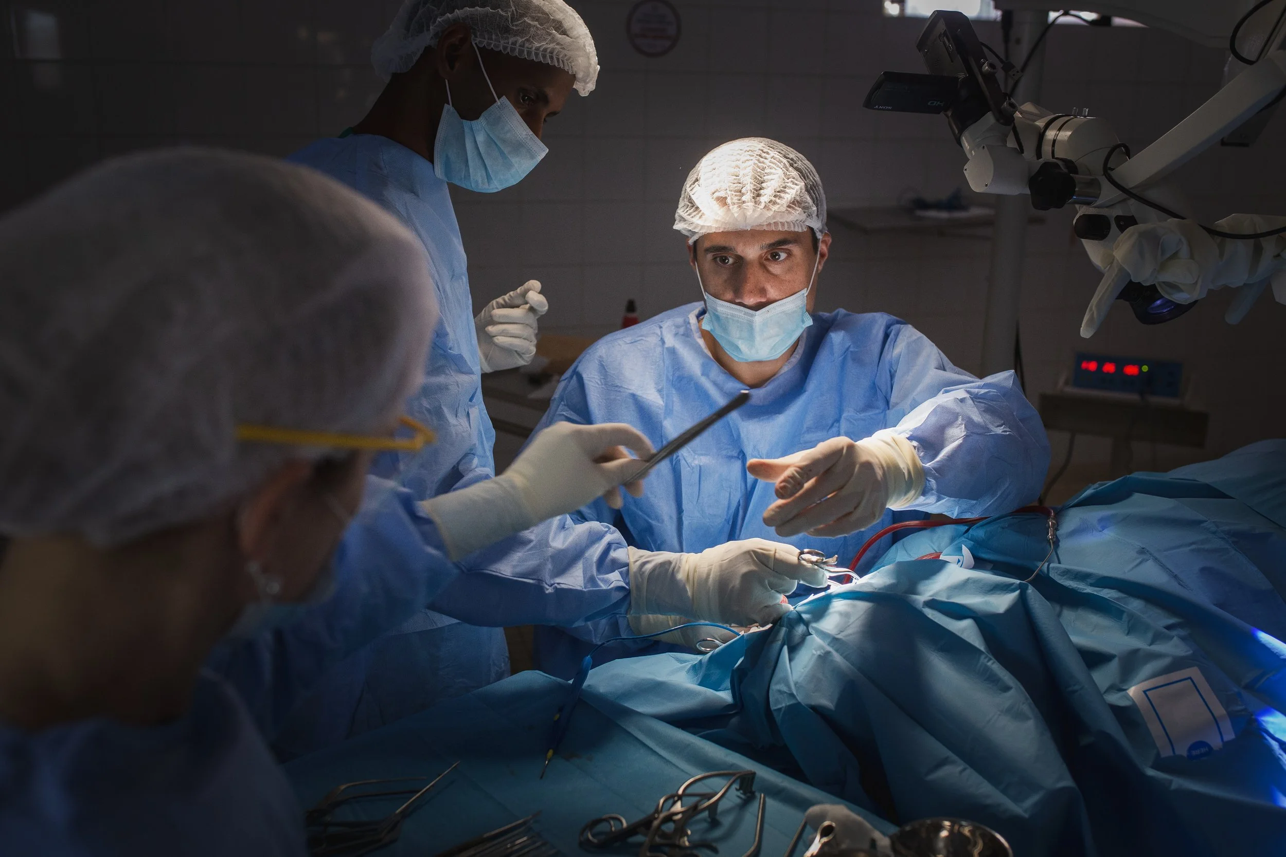 Medical team performing surgery in an operating room with surgeons wearing scrubs, masks, and gloves, focused on the patient.