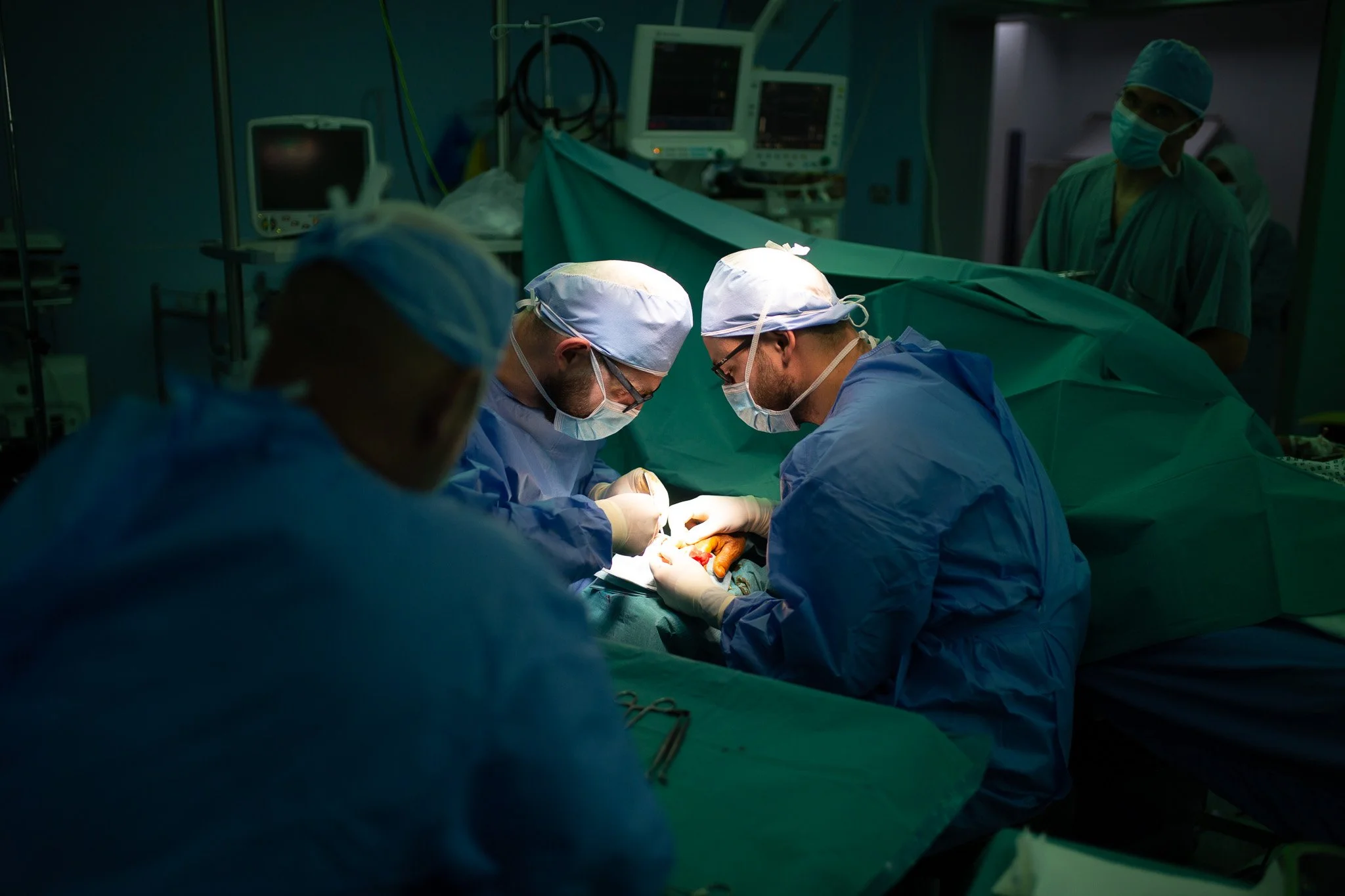 Surgeons in an operating room performing surgery with medical monitors in the background.