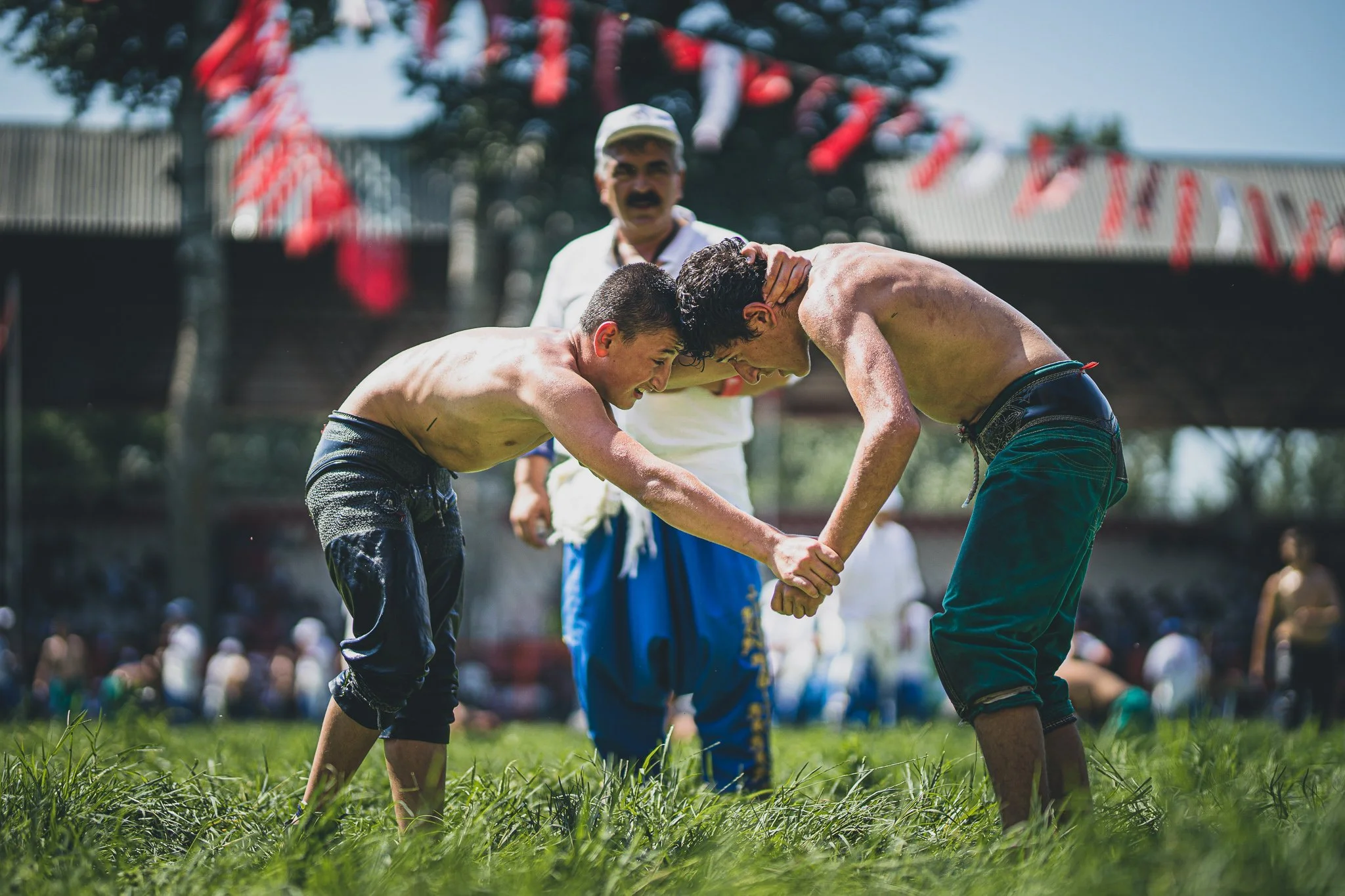 Two men wrestling in a traditional Mexican sport called Lucha Libre, with a referee in the background during a match.