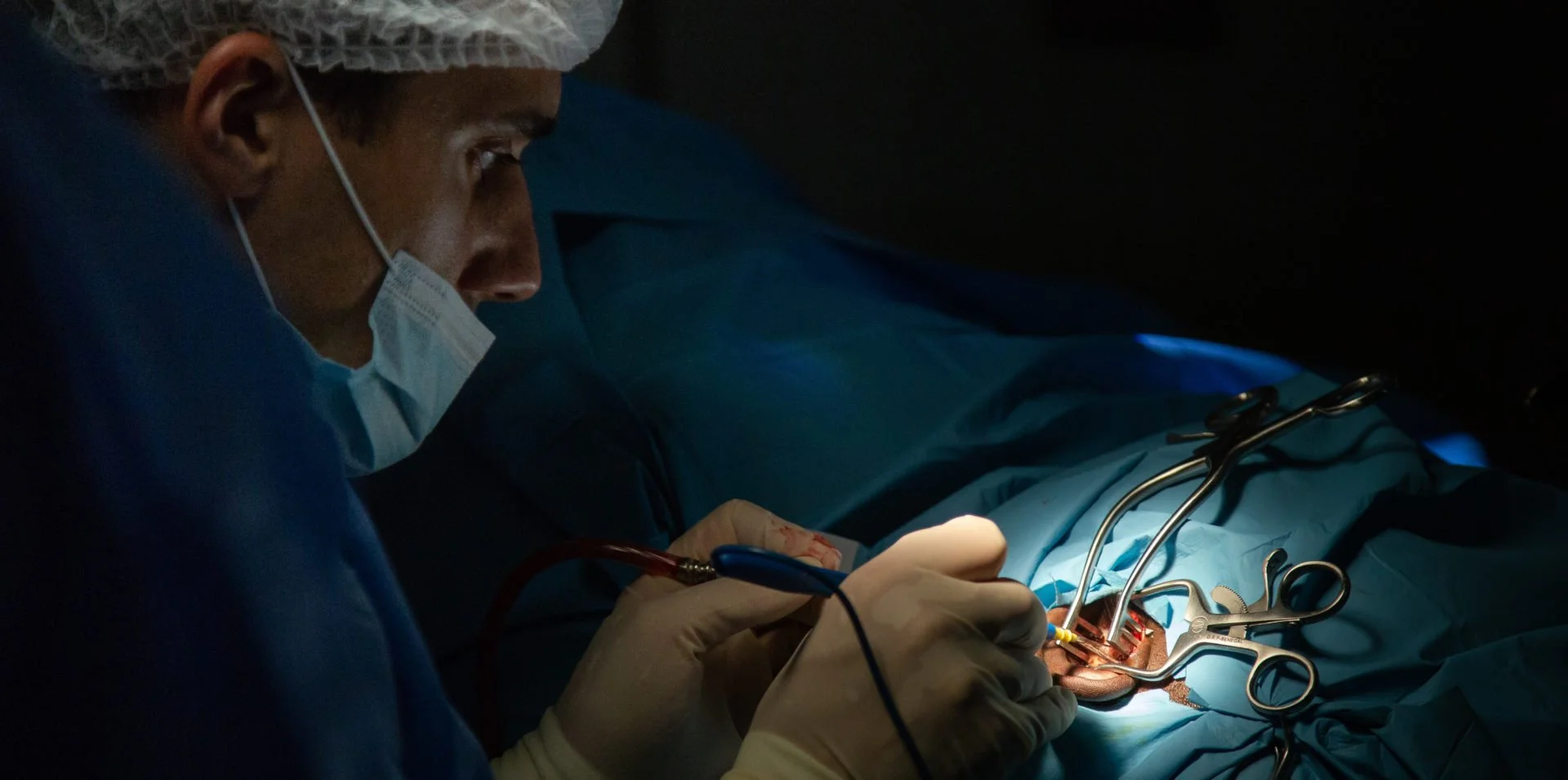 Surgeon performing surgery in a dark operating room with surgical tools and a patient.