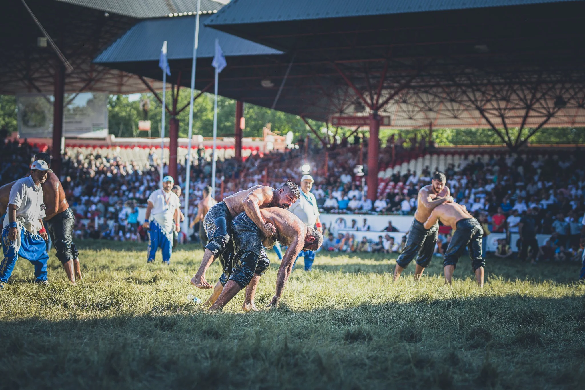Two men wrestling on a grassy field during a competitive match with spectators in the background.