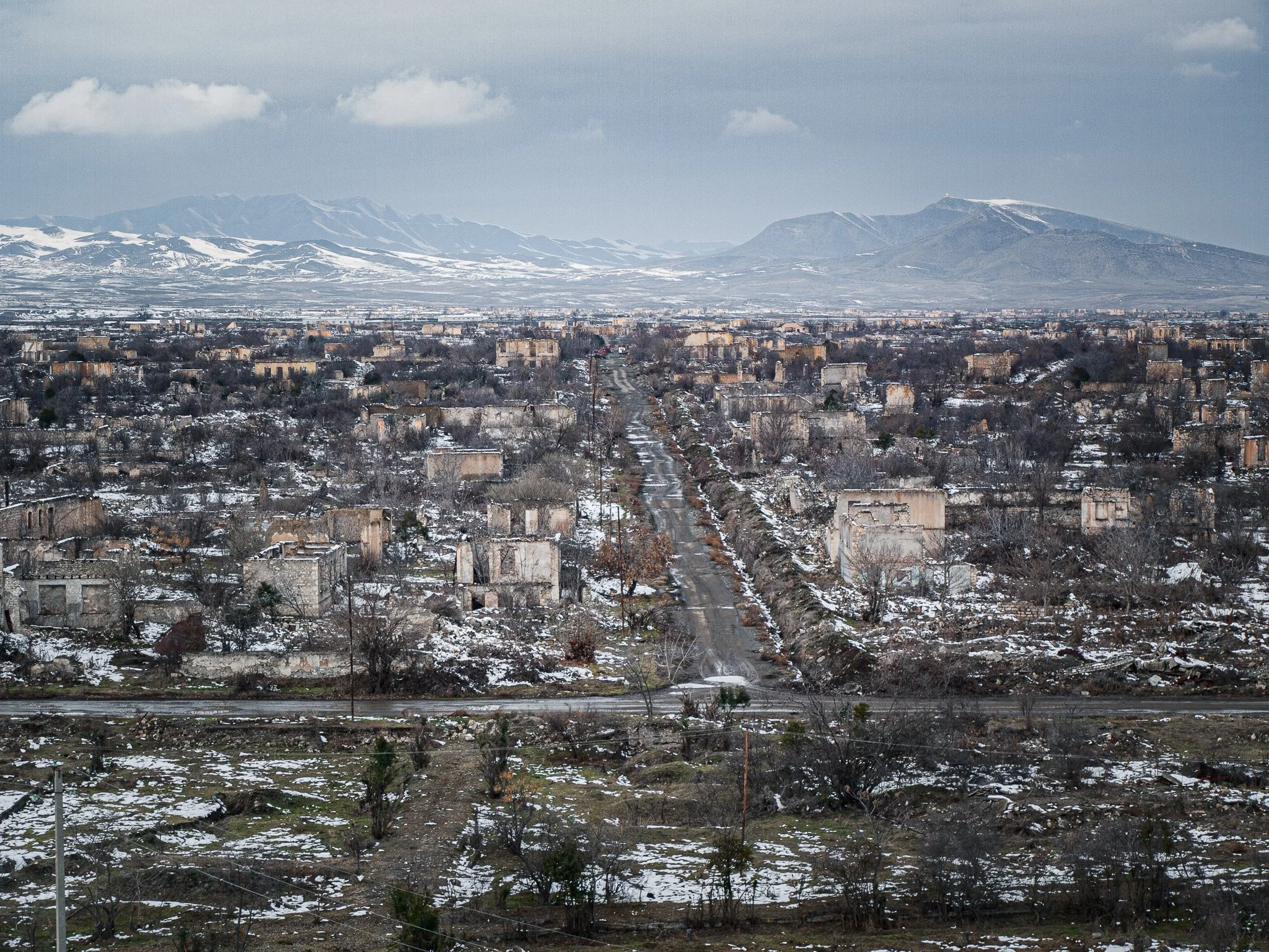 Ruined buildings and winter landscape with snow-covered ground and mountains in the background.