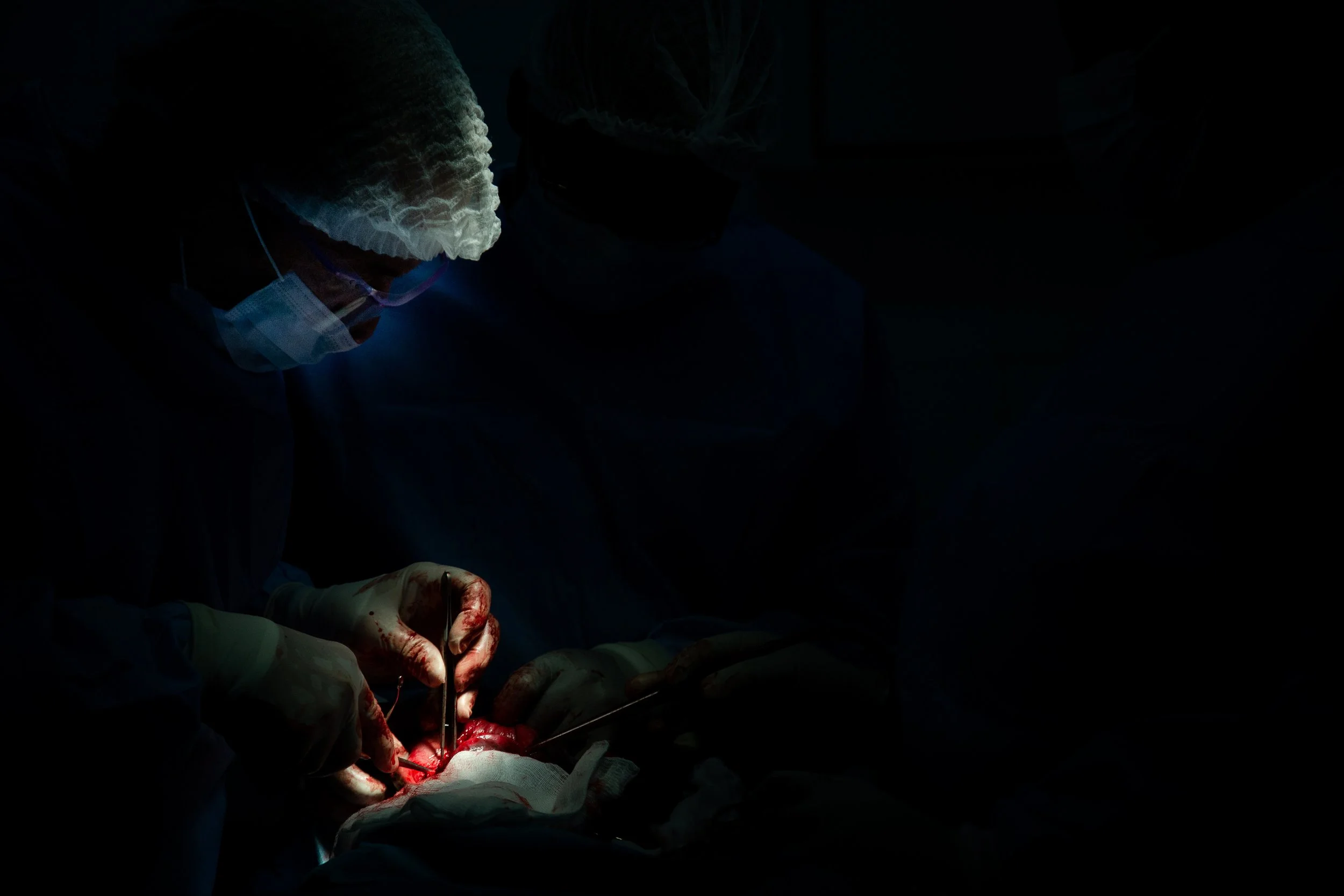 Surgeons performing an operation in a darkly lit operating room, focusing on the surgical area.
