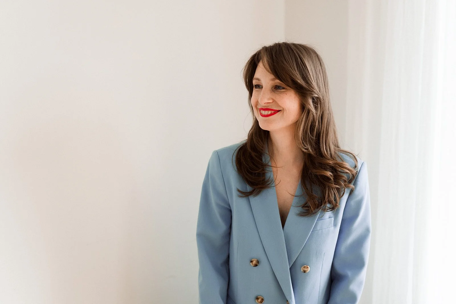 Eine lachende Frau in einem blauen Blazer vor hellem Hintergrund.