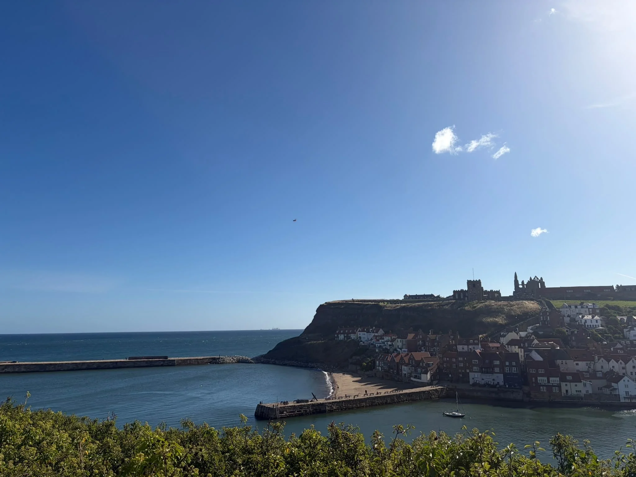A coastal town with houses along the shoreline, a castle on a hill, and a bright blue sky with a few clouds.