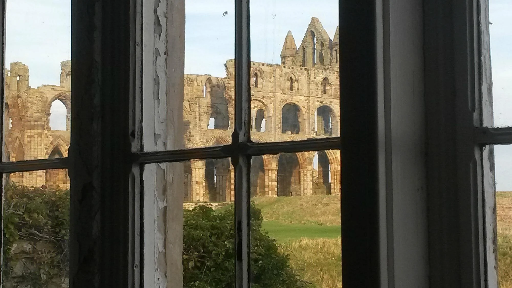 View of ancient stone ruins, likely a cathedral or castle, seen through a window with peeling paint and black framing.