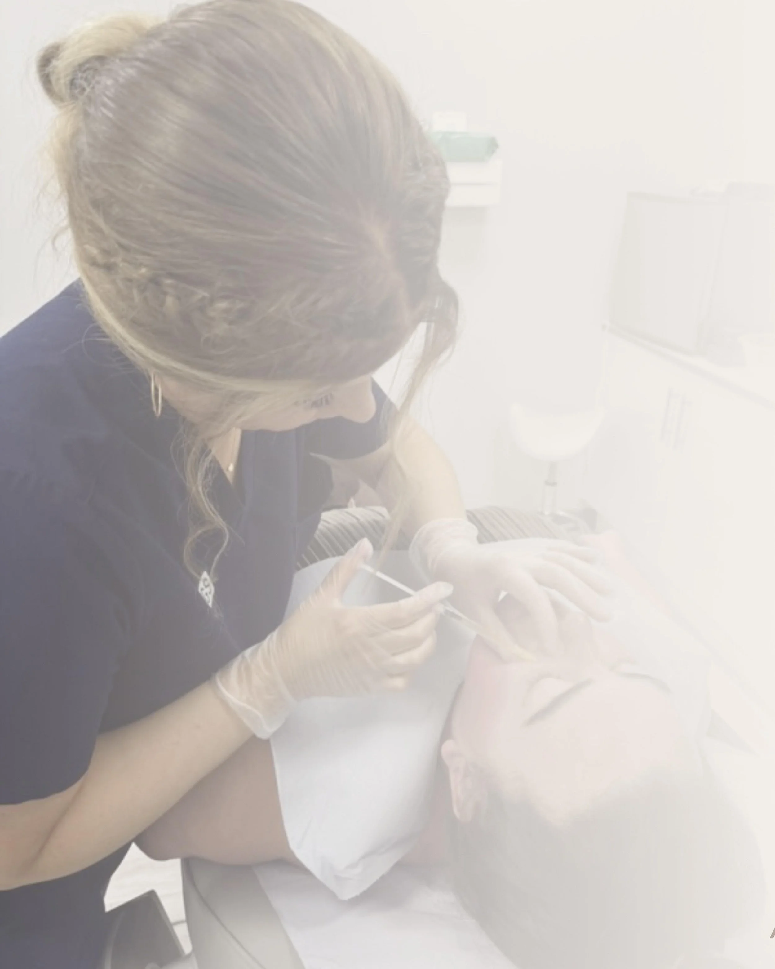 A woman receiving a cosmetic treatment on her face in a clinical setting, with a technician applying a procedure while both wear gloves.