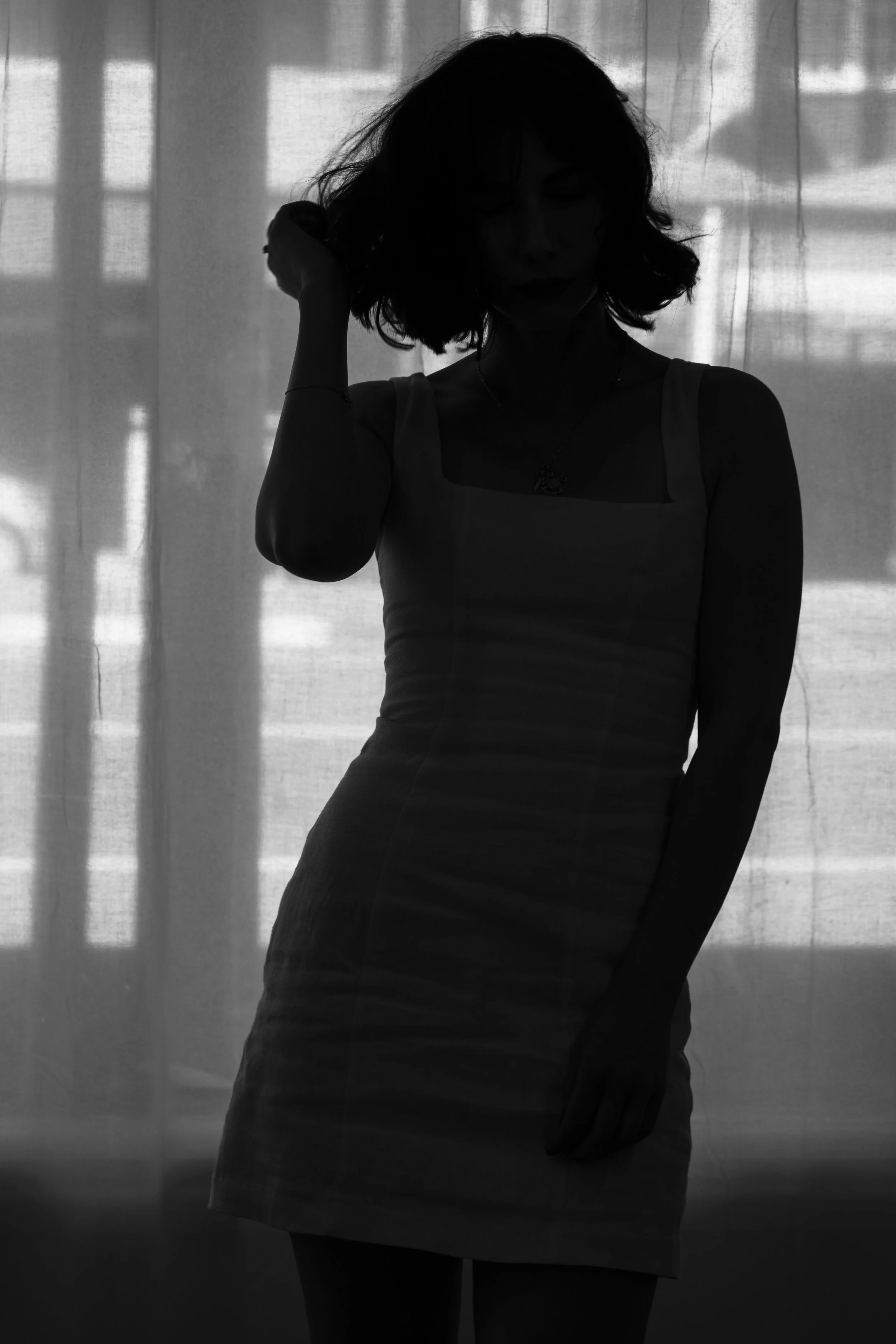 Silhouette of a woman with short hair standing in front of a light-colored curtain.