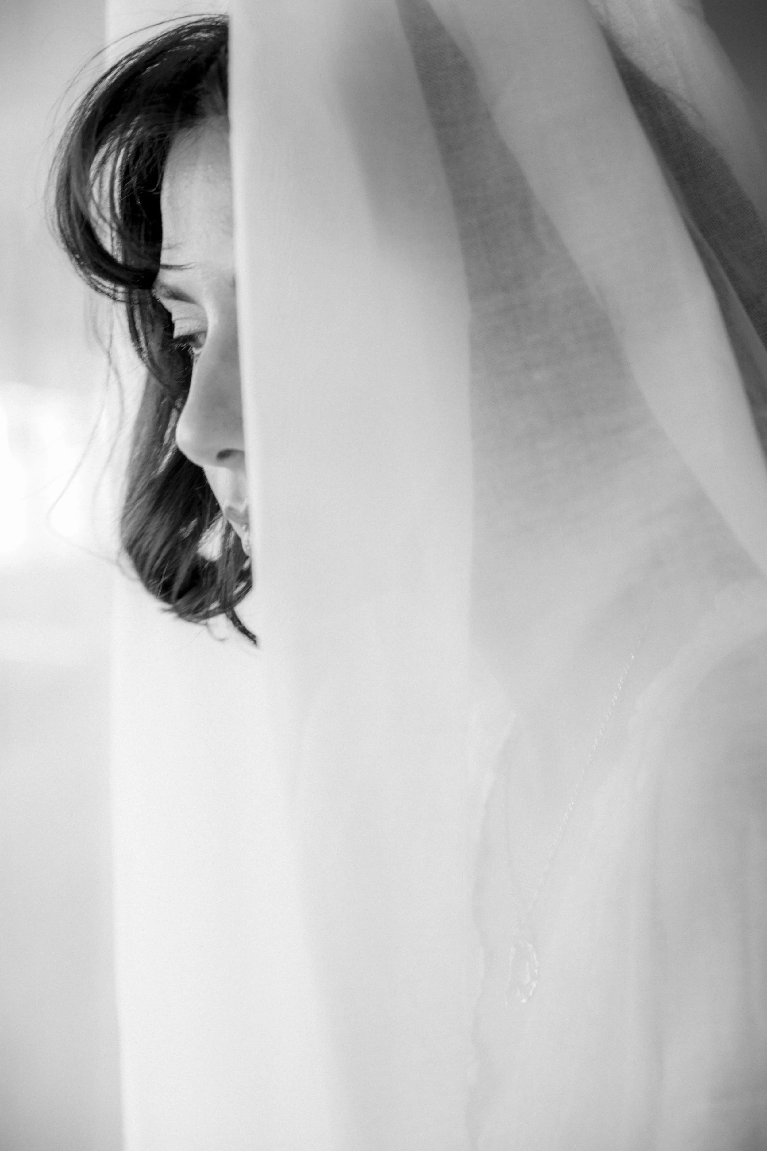 Close-up of a person's face seen through a partially closed door, with only one eye and part of their nose and mouth visible, in black and white.