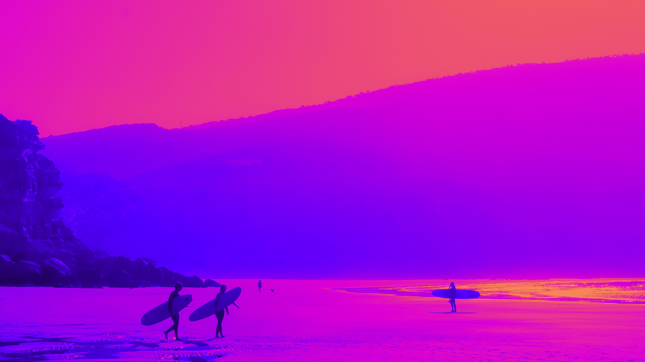 Surfers walking on a beach holding surfboards, with one surfer carrying their surfboard under their arm, during sunset with a colorful sky.