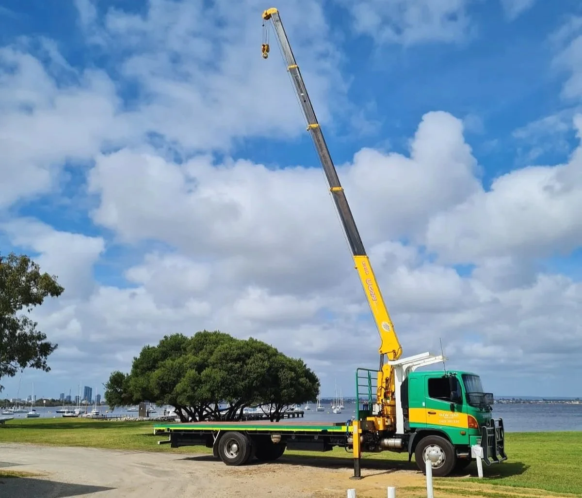 image is of a Green and Gold Hiab truck in Perth Western Australia with the boom fully extended. The Swan River is in the background.