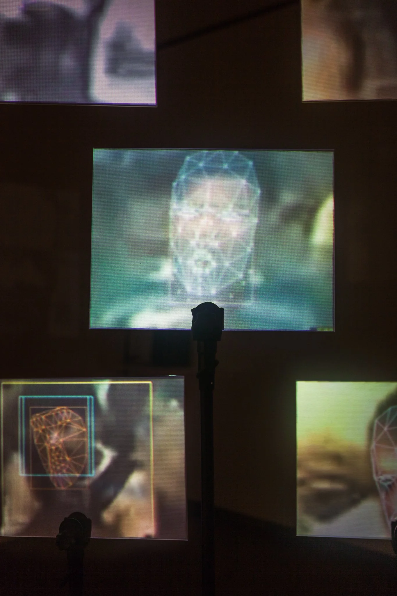 Projection screens displaying images of digital human faces with wireframe designs, with stage lights and dark room background. Digital Art