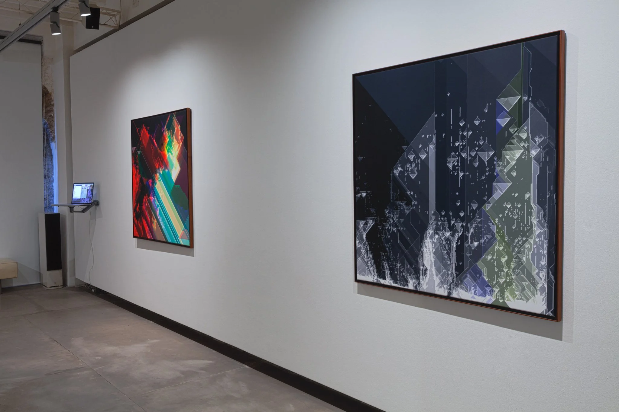 Two abstract, digital-style paintings hung on a white gallery wall, with a small monitor displaying an image or information nearby.