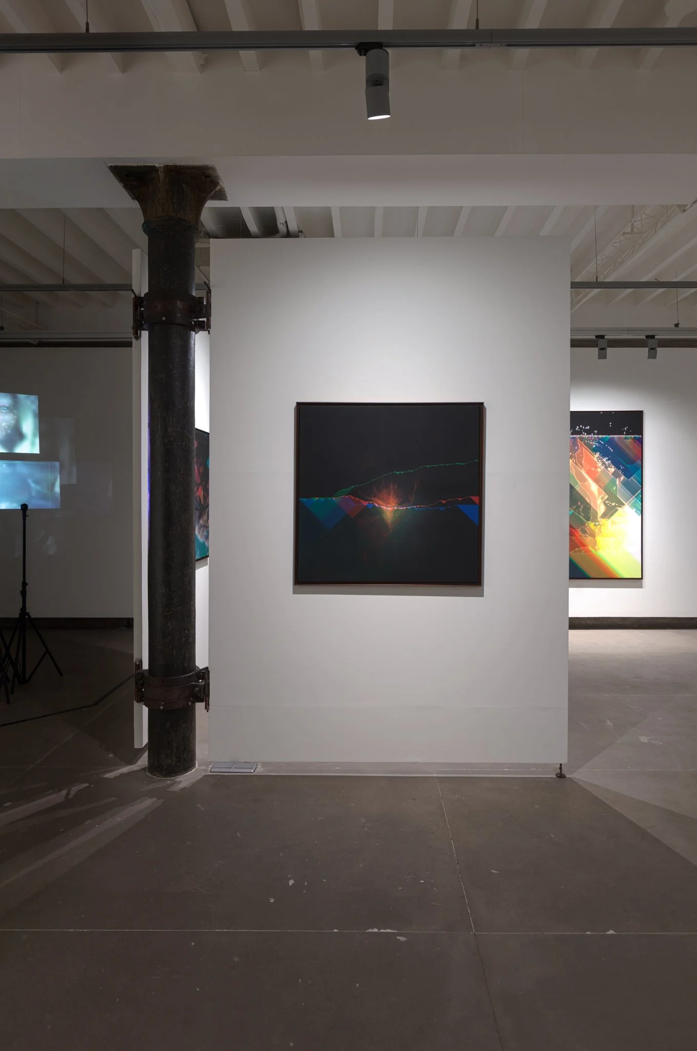 Abstract digital artwork with dark background and colorful light lines and shapes, displayed on a white wall in an art gallery.