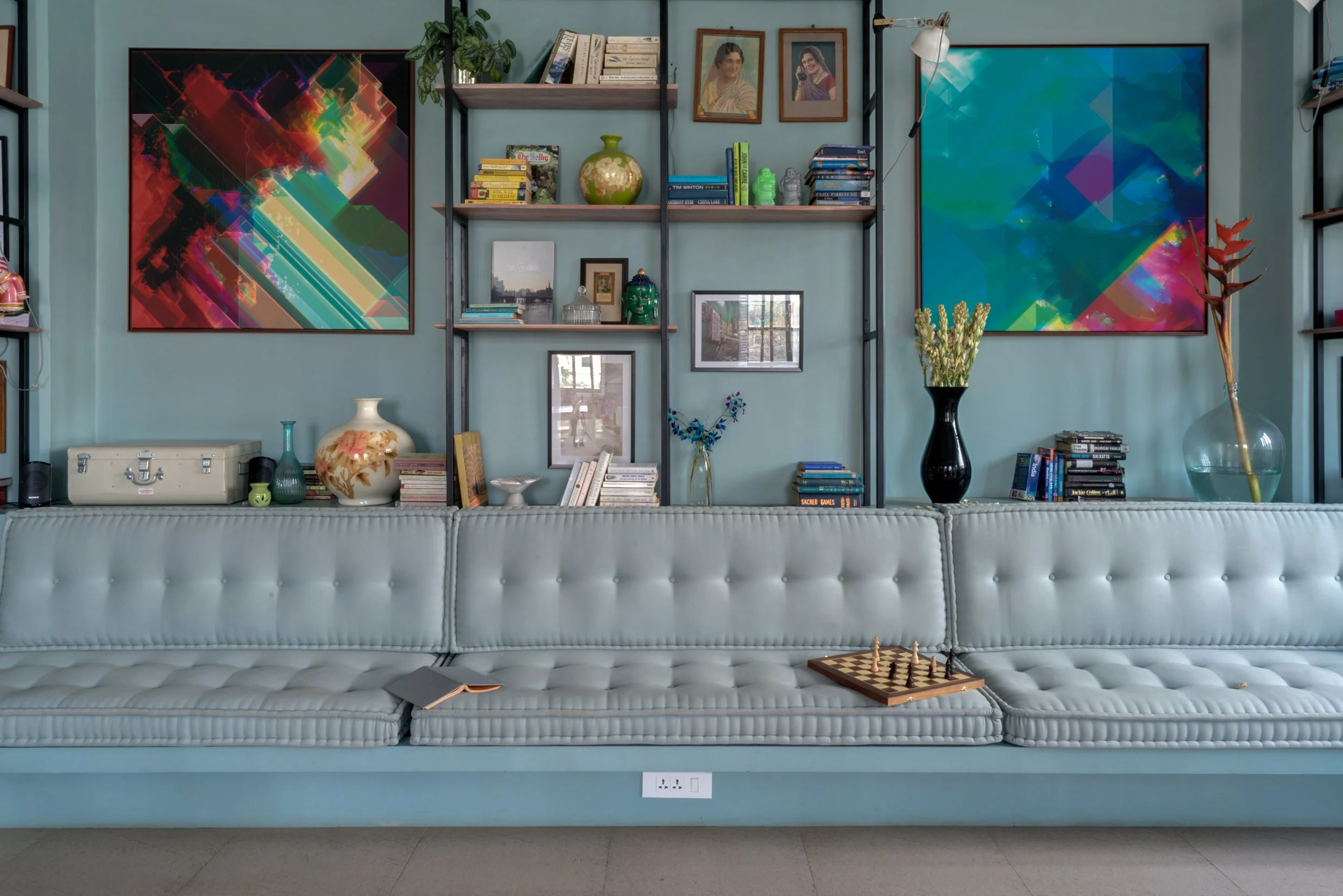 Living room with a pastel-colored tufted sofa, bookshelves, framed artwork, vases, and decorative objects on a wall.