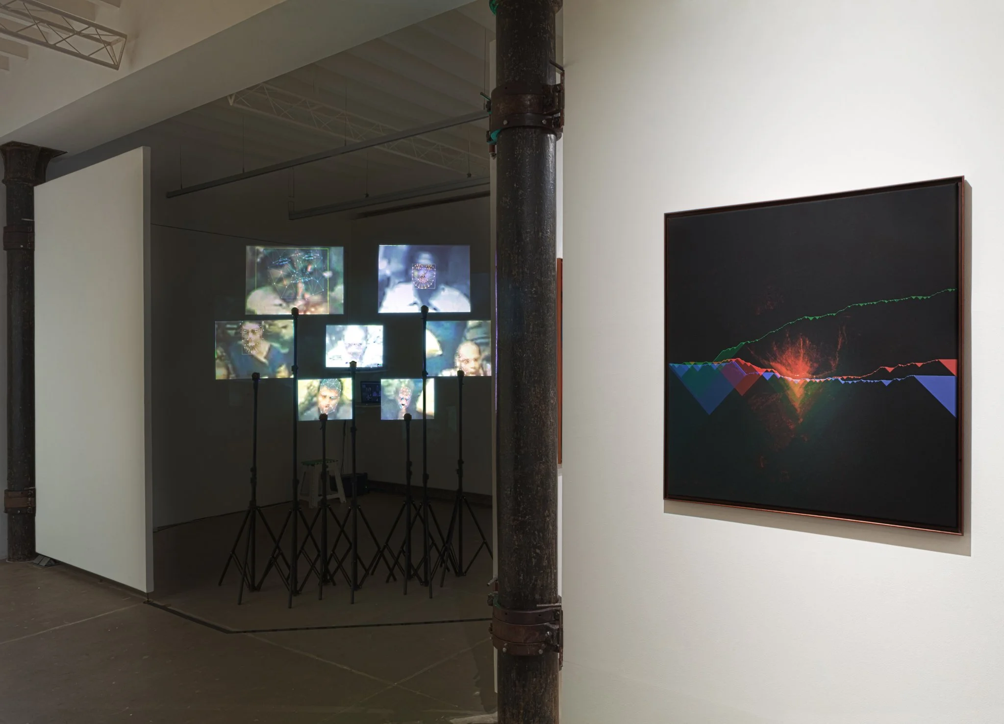Art installation with multiple screens displaying faces and a dark digital graph print on the wall.