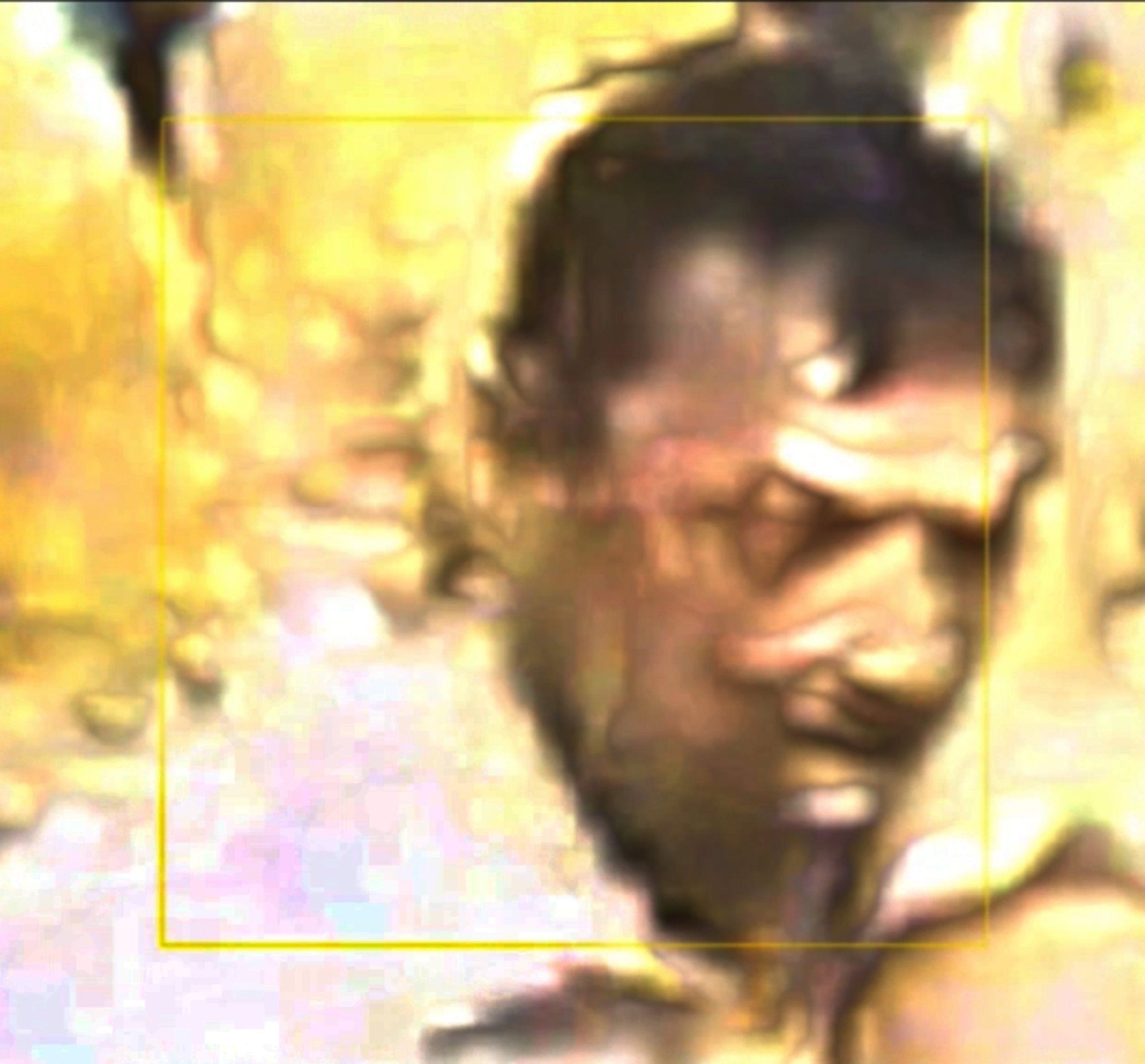 A blurry, dark-skinned young person's face with a smile, dark curly hair, and bright eyes, set against a yellowish background. Digital Art. Generative Art. Face detection