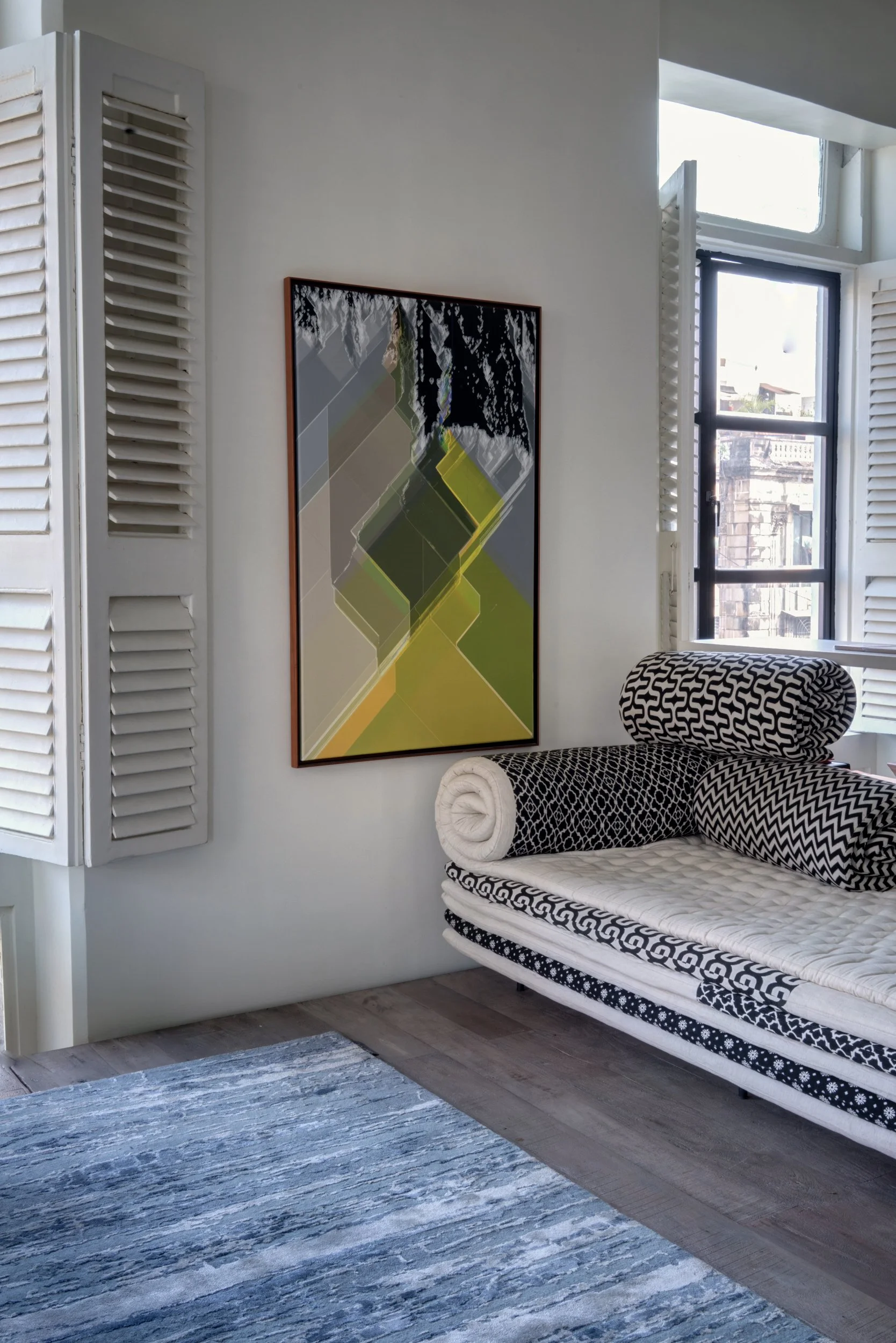 Interior corner of a room with a black and white patterned daybed, abstract artwork on the wall, and wooden floors with a blue and white rug.