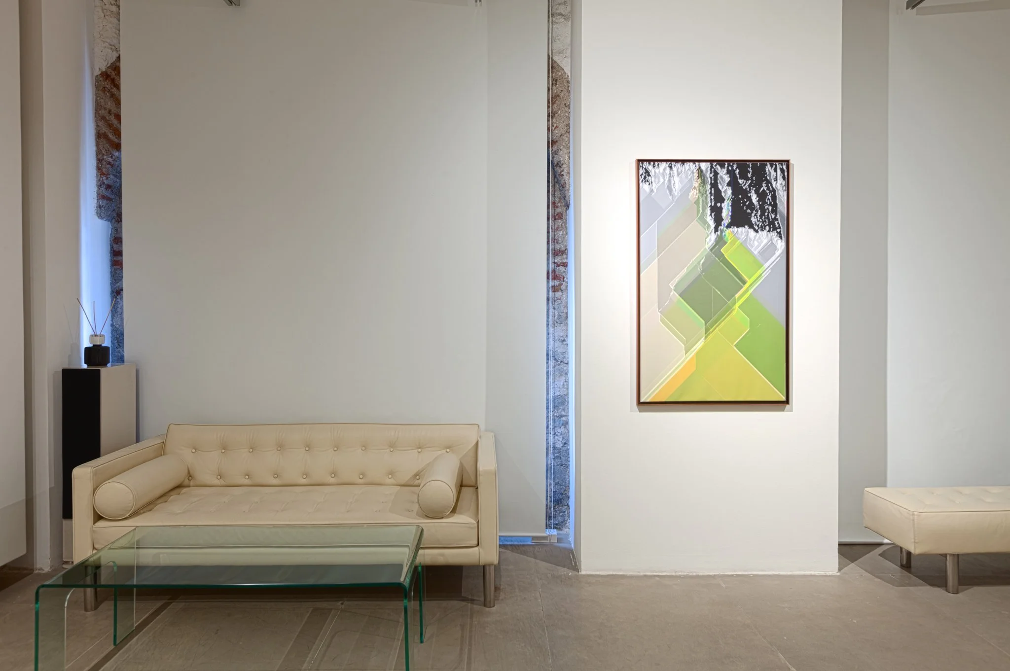 Modern minimalist living room with cream sofa, glass coffee table, and abstract artwork on white wall.