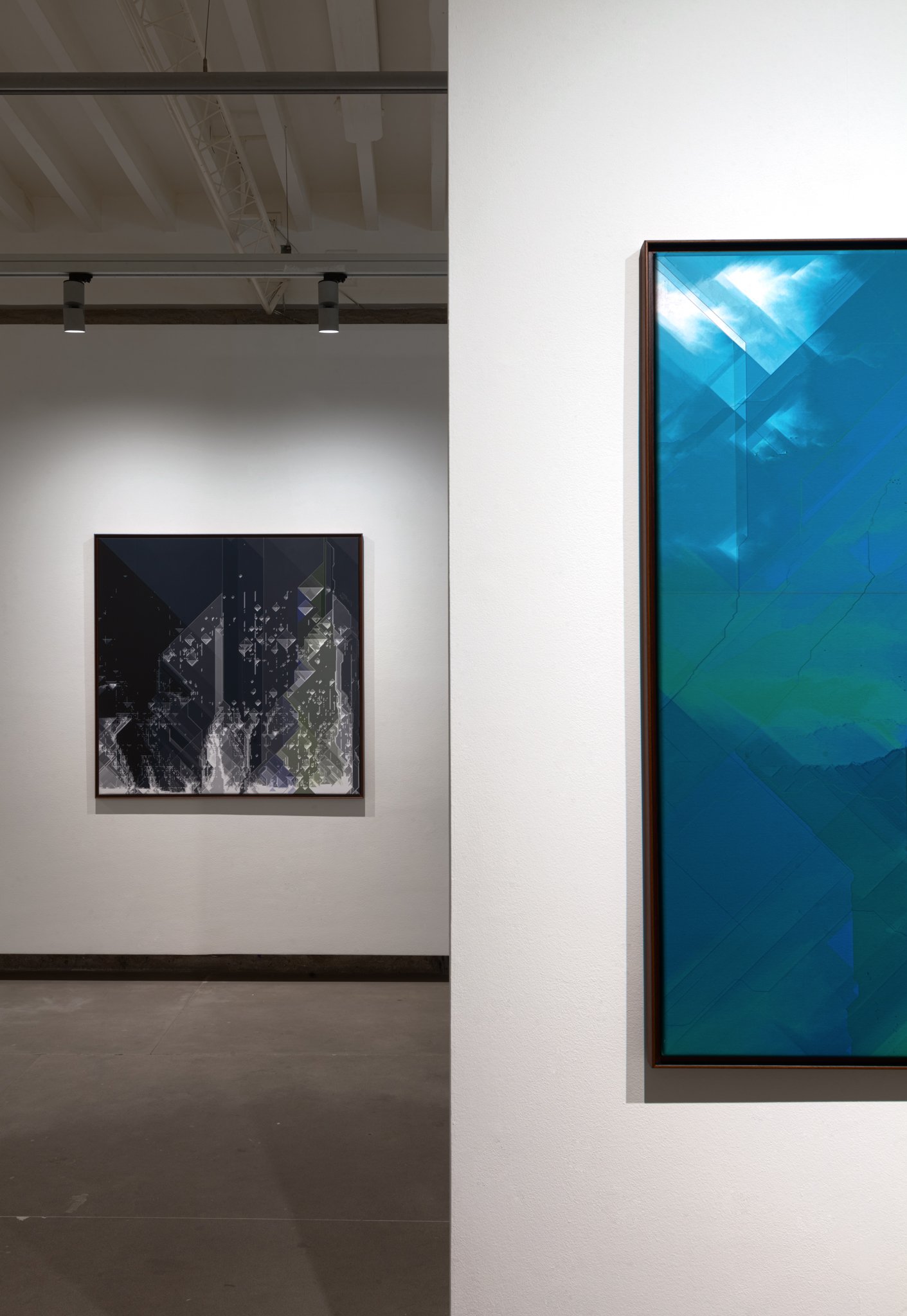 An art gallery display with two abstract paintings, one predominantly black and white on the left wall, and one vibrant blue on the right wall, with overhead lighting highlighting the artwork.