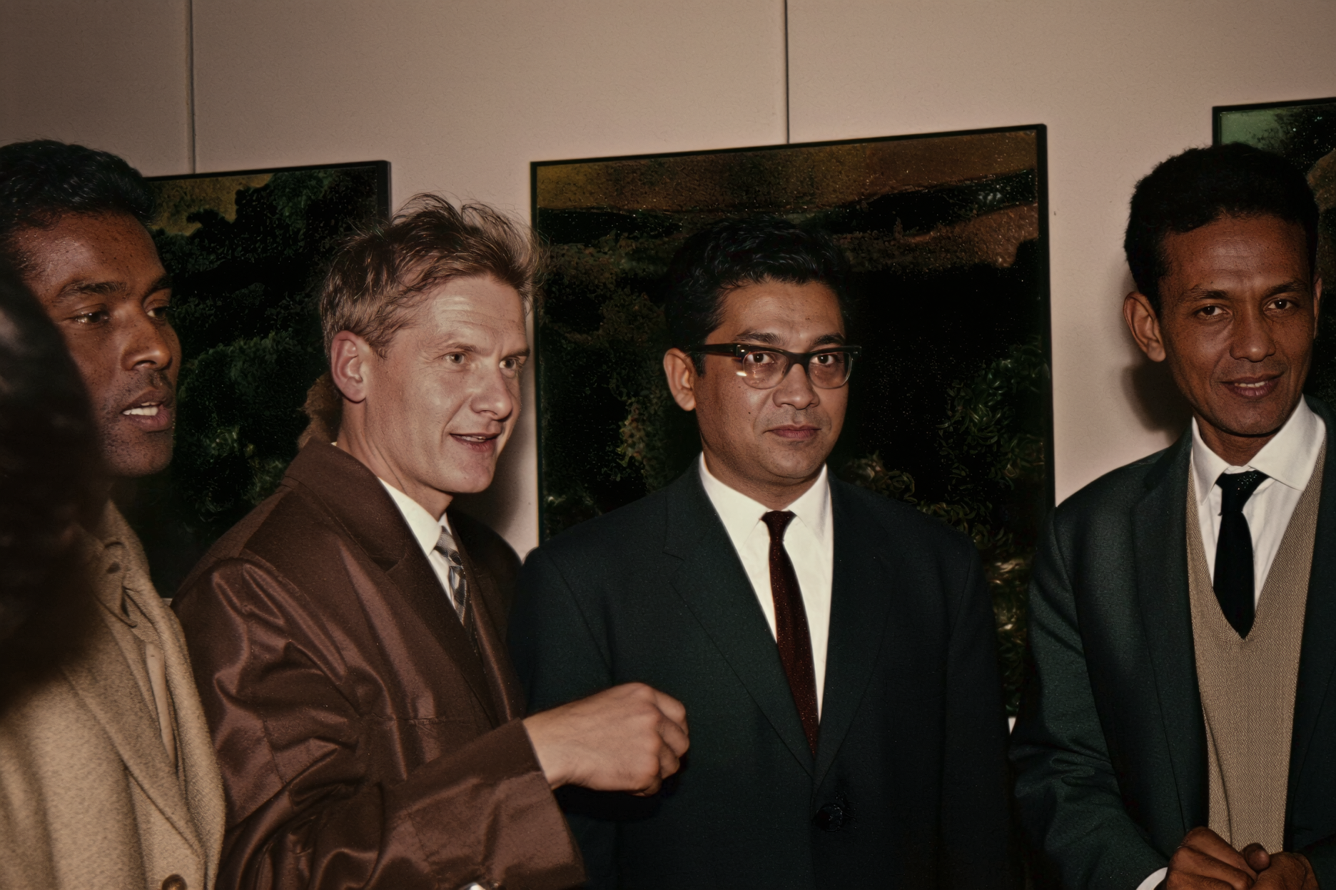 Four men in formal attire standing together at an art exhibition or gallery, with framed landscape photographs hanging on the wall behind them.