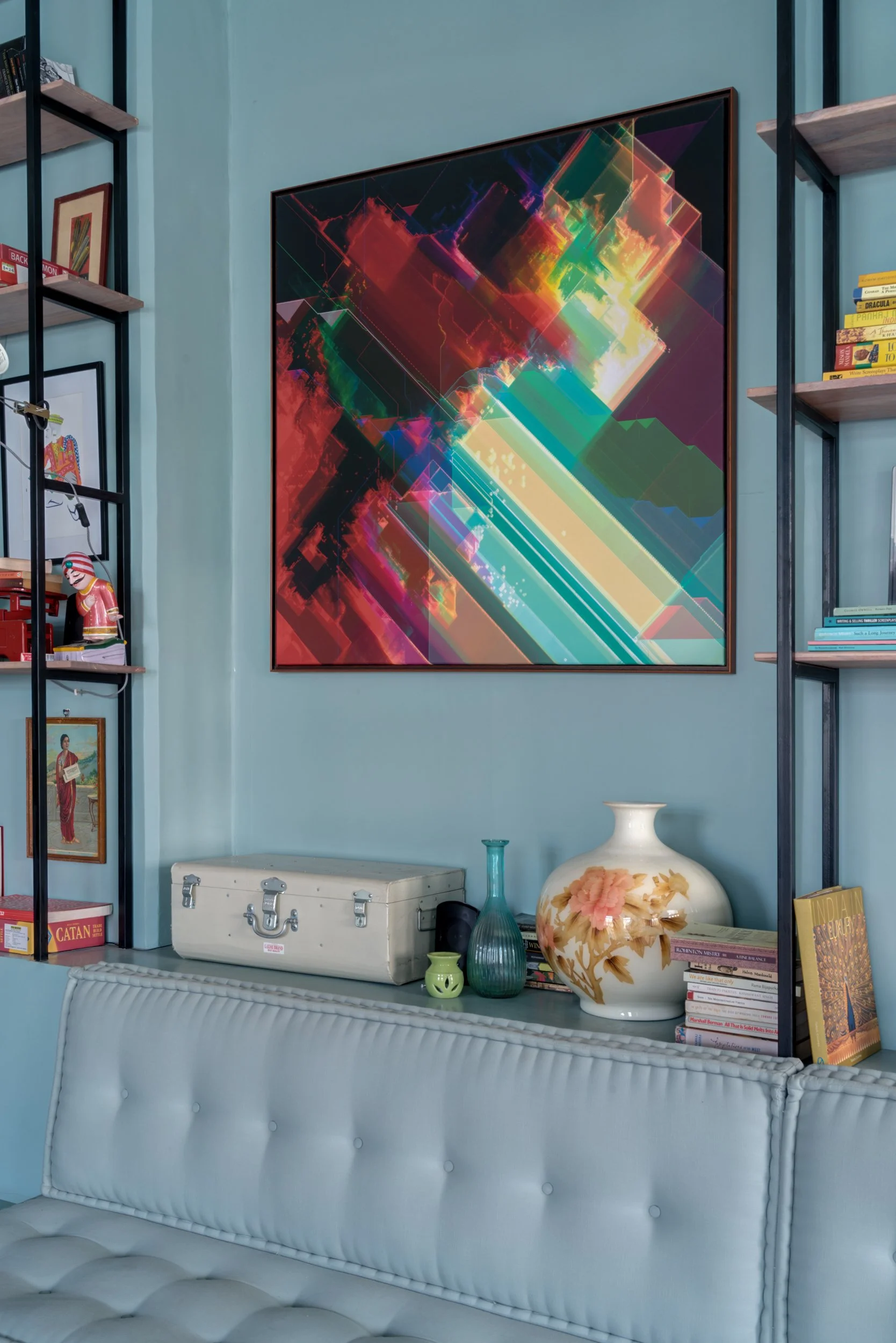 Decorative living room corner with colorful abstract artwork on the wall, shelves with books and decorative items, and a tufted white sofa.