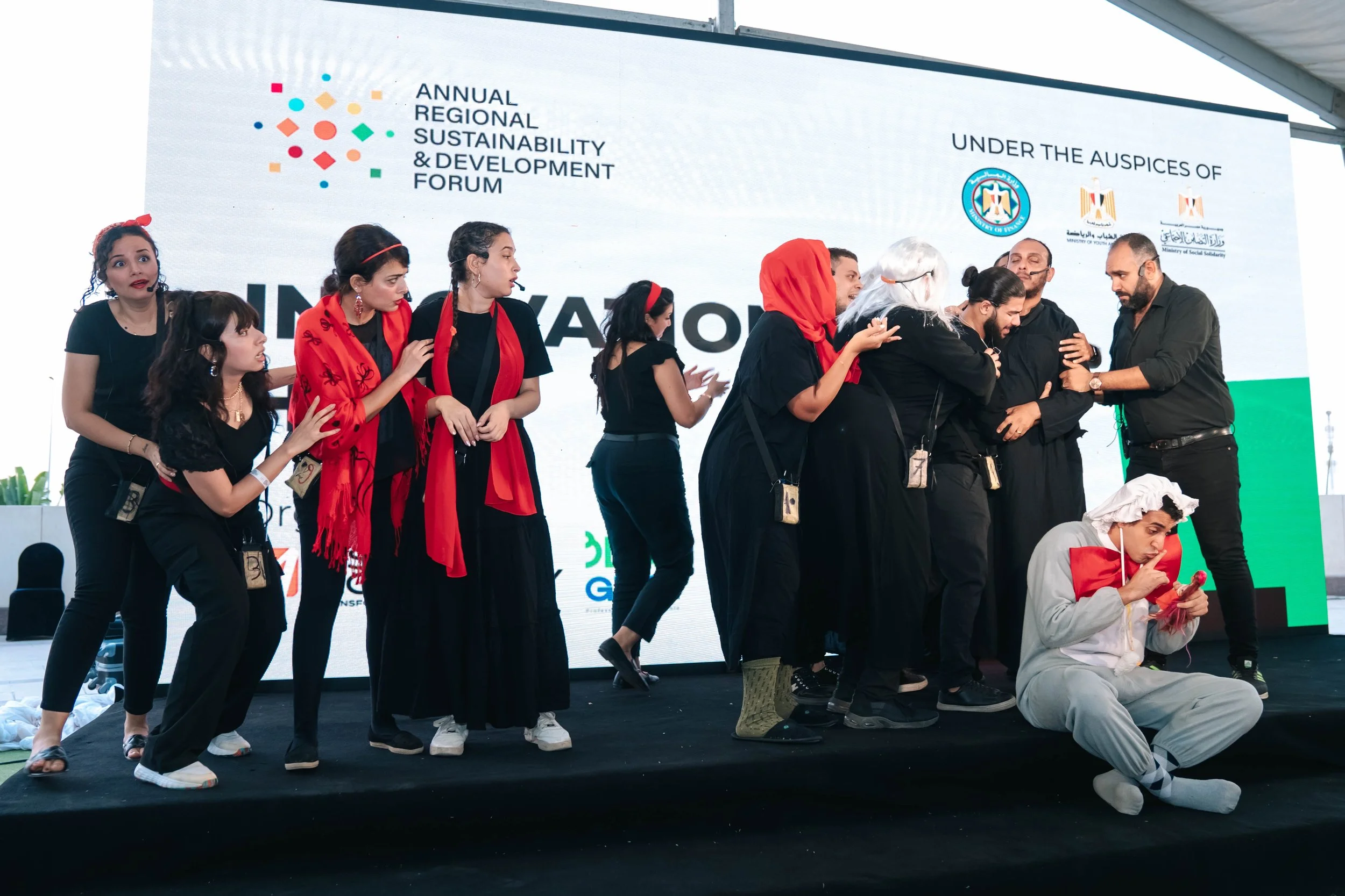 A group of actors on stage during a performance at the Regional Sustainable Development Forum, First Edition, with a large event banner in the background.
