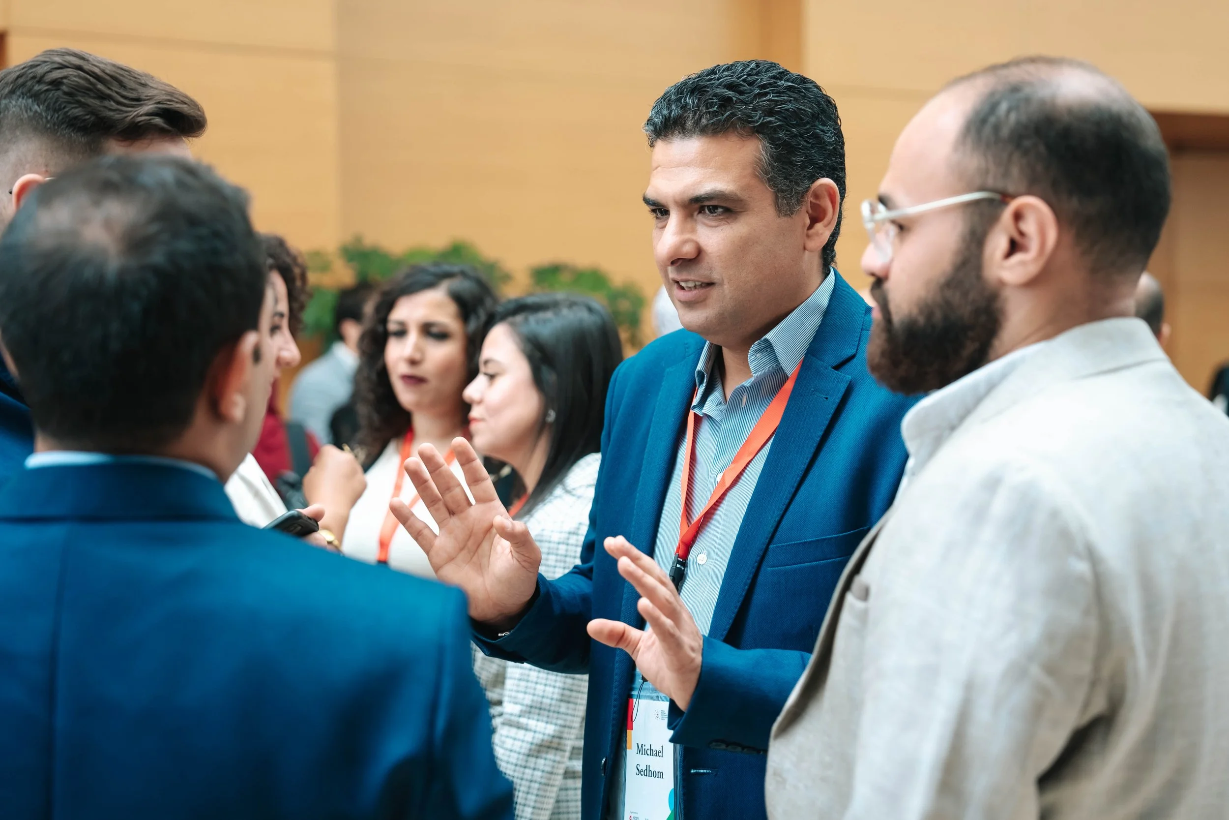 Group of professionals engaging in a discussion at a conference, with a man in a blue suit speaking to a small group of colleagues at the Regional Sustainable Development Forum, First Edition.