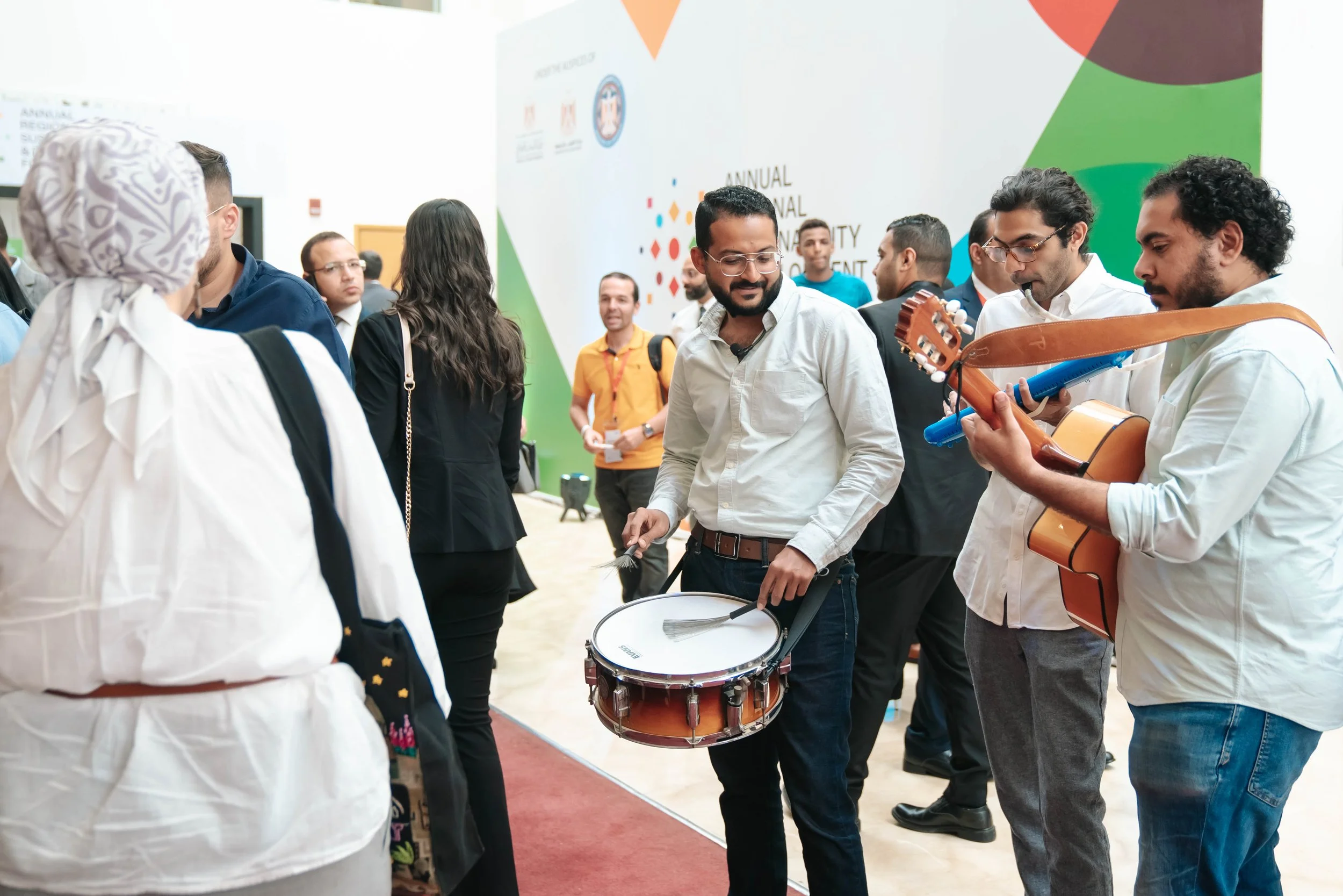 People playing musical instruments at the busy Regional Sustainable Development Forum, First Edition, with a large colorful wall in the background.